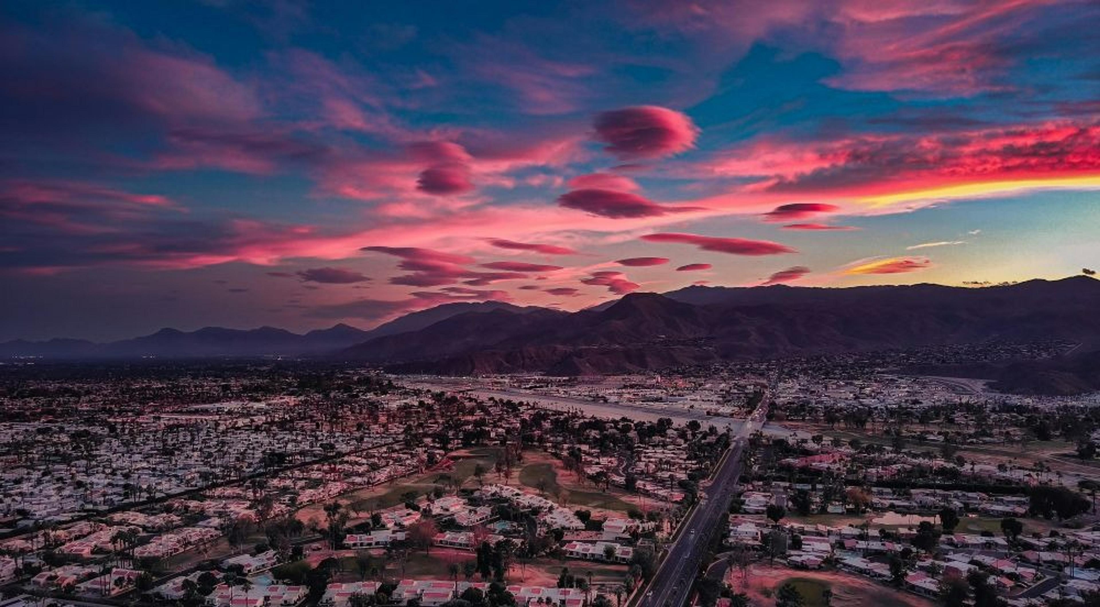 A stunning pink sunset casts vibrant colors over the cityscape of Palm Springs, California, with mountains in the background.