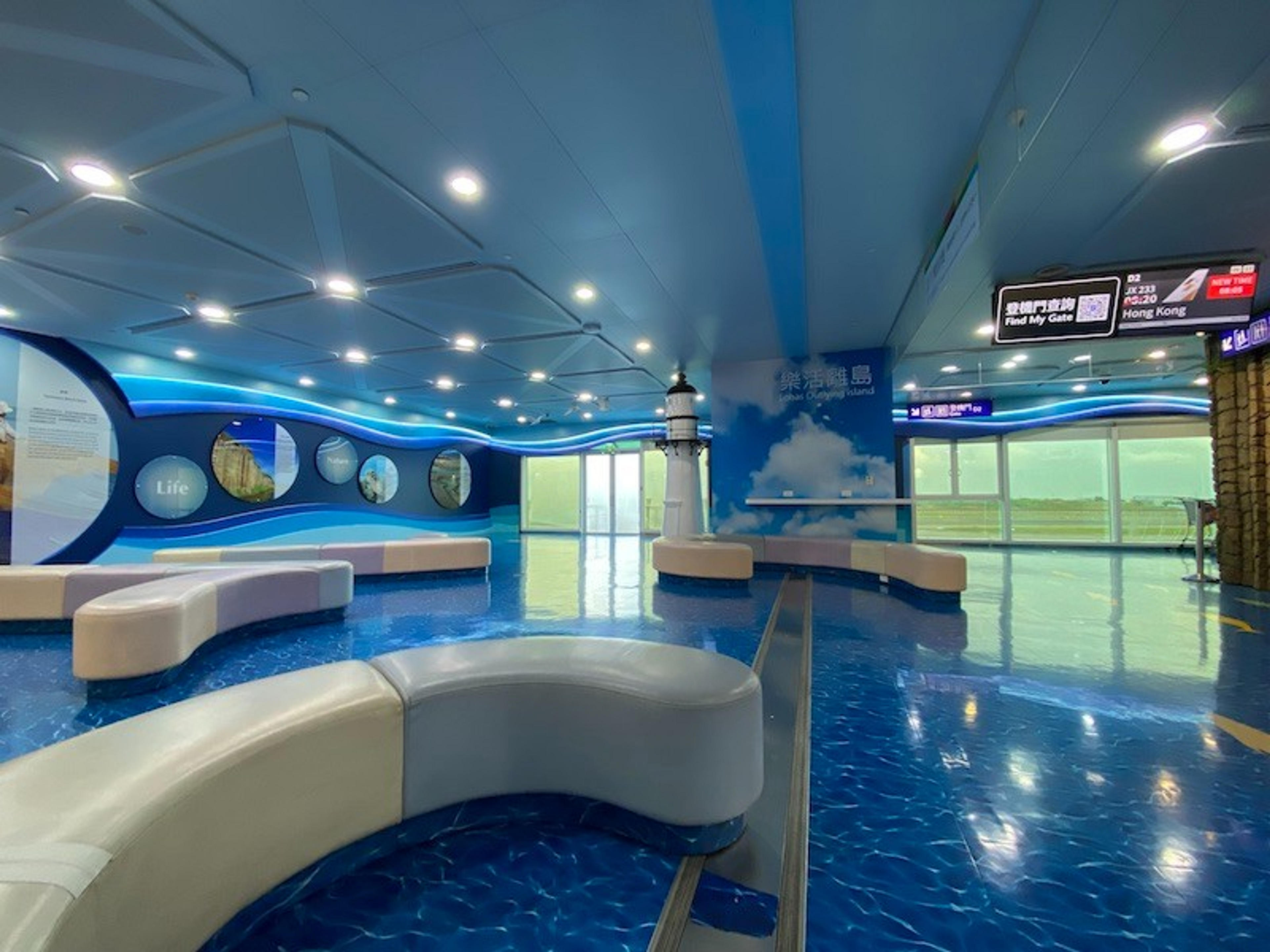 Inside Taipei Airport, a bright and modern waiting area features ocean-themed decor and a lighthouse structure.
