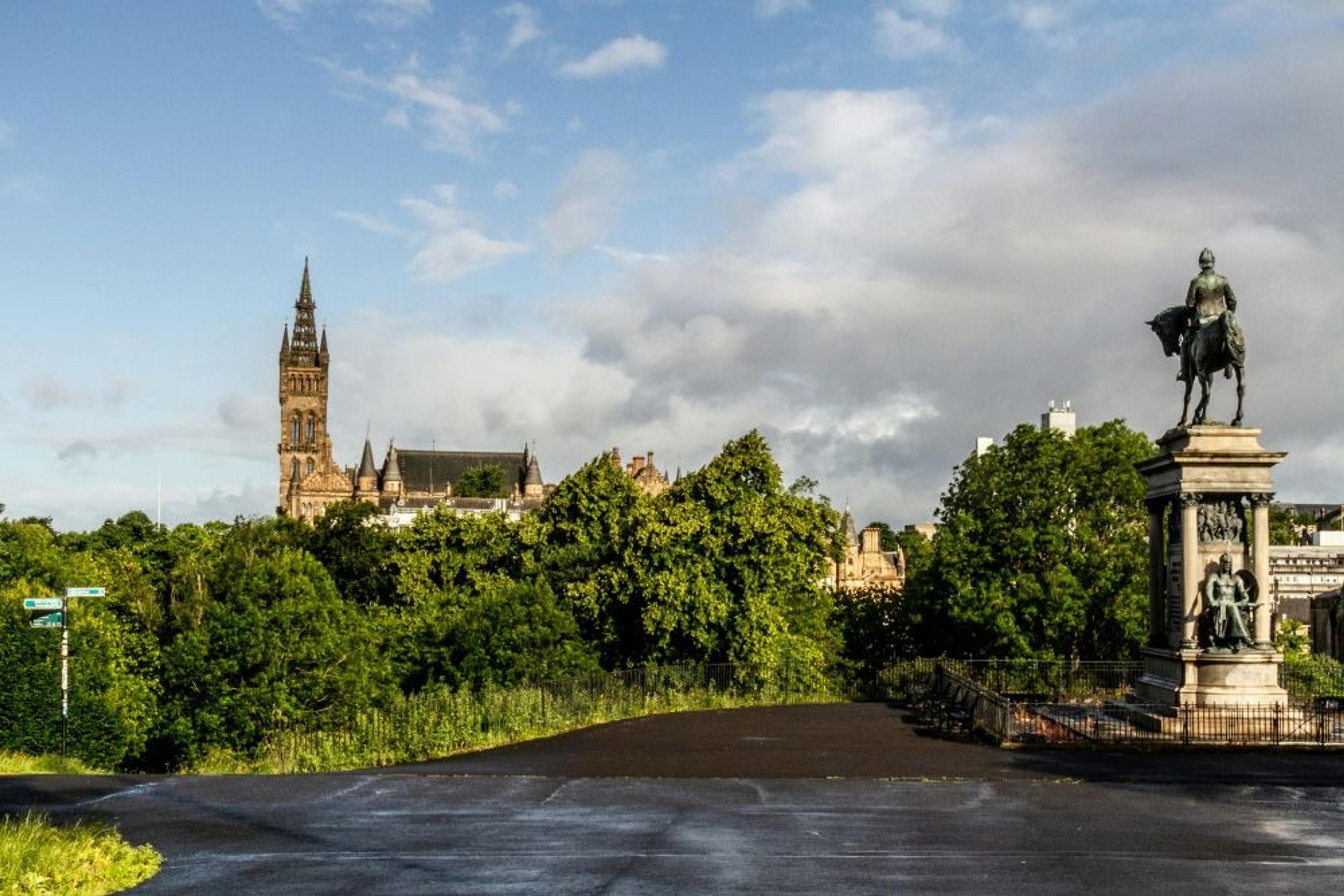 A scenic view of the University of Glasgow, featuring its iconic tower and a nearby equestrian statue.