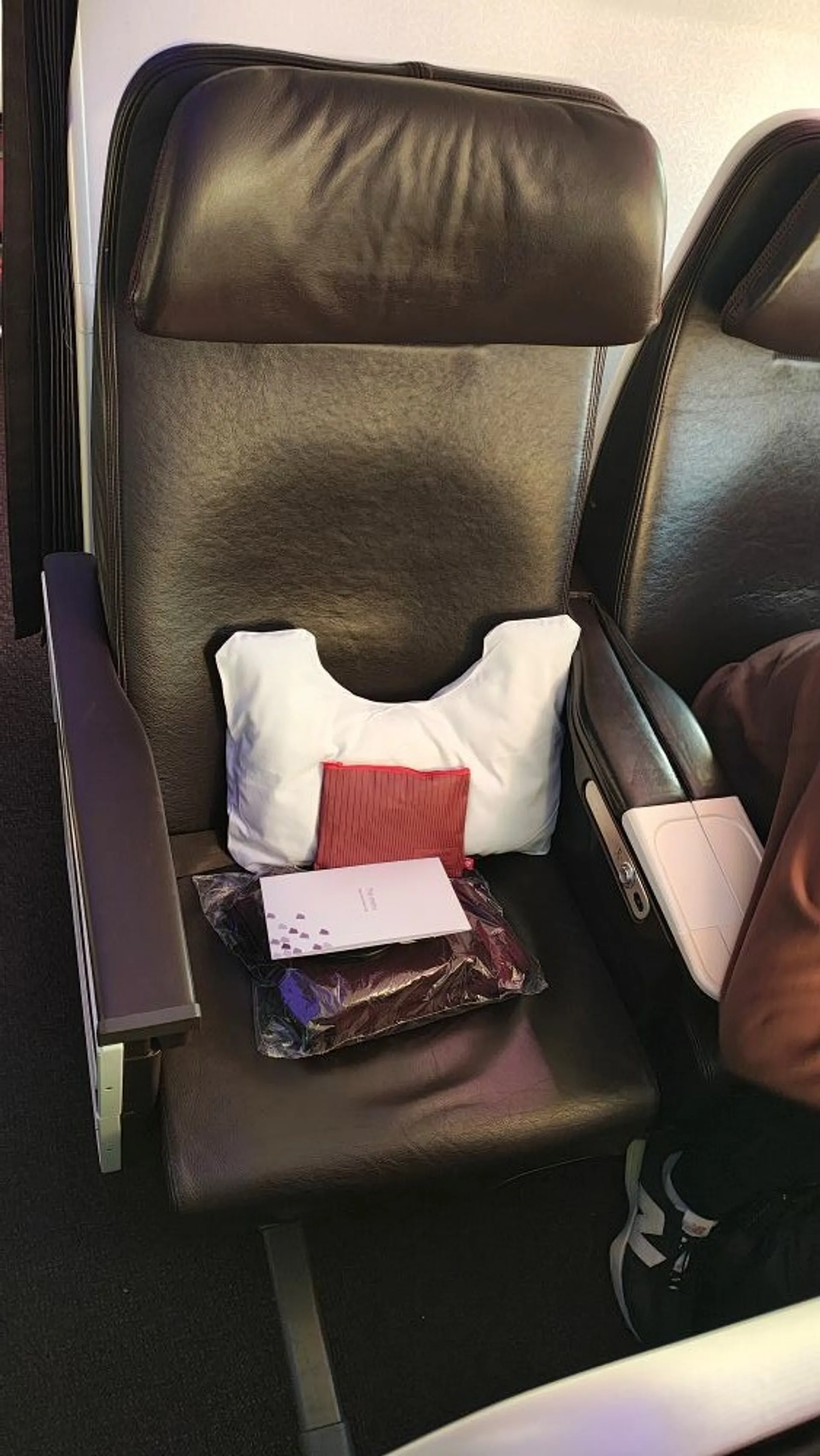 A business class airline seat with travel amenities, including a pillow, amenity kit, and menu, on Virgin Atlantic Premium economy
