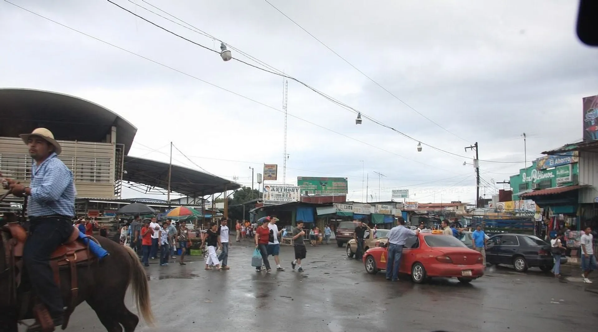 A bustling street scene unfolds in the border town of Paso Canoas 
featuring a man on horseback and lively market activity.