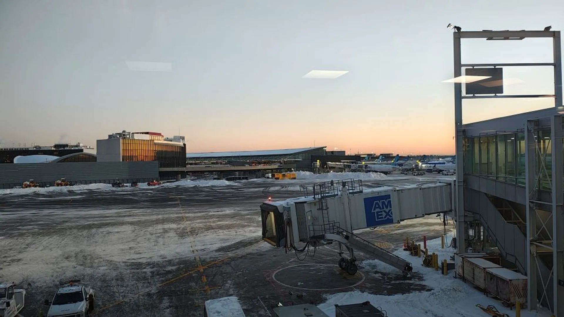A snowy JFK Airport at dawn with an empty jet bridge extending from the terminal.