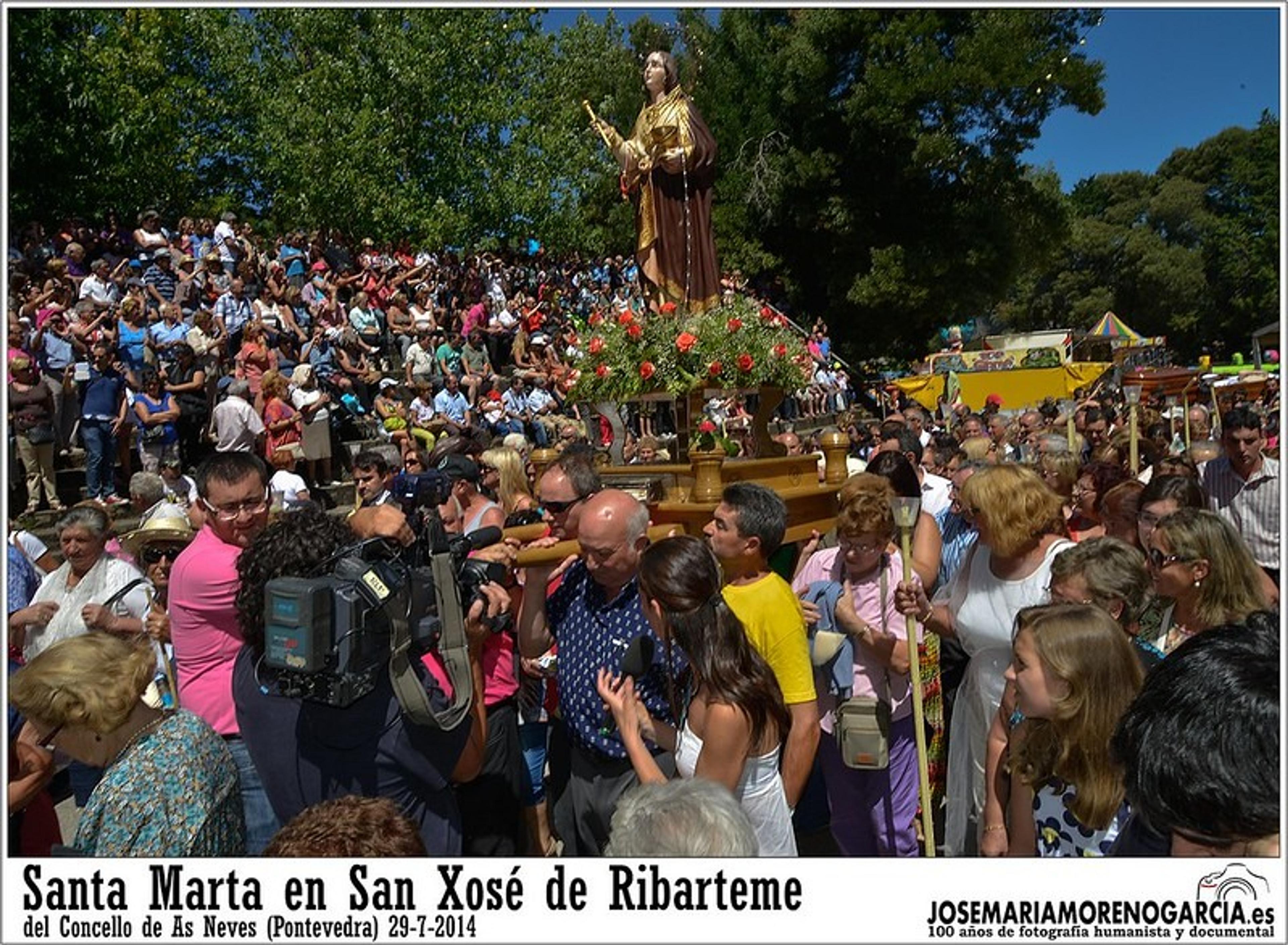 A festive crowd gathers around a statue adorned with flowers in San Xosé de Ribarteme, Pontevedra.