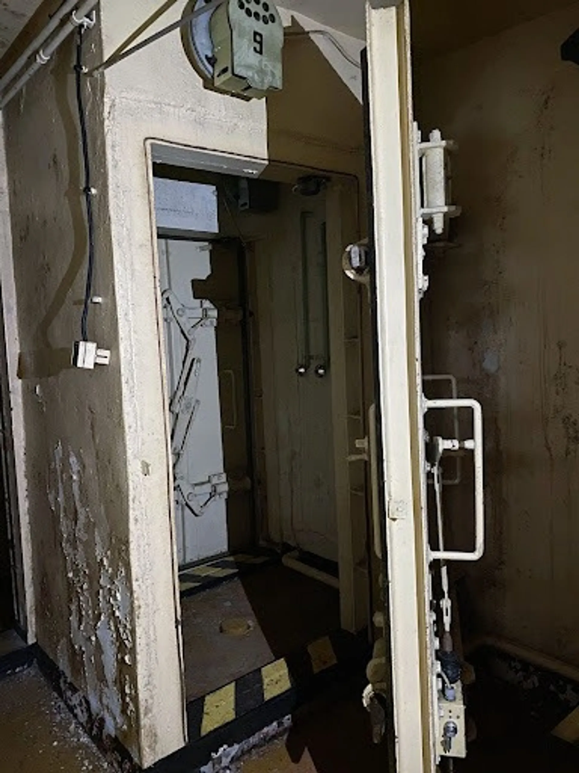 An abandoned radiation decontamination shower room in a Cold War-era bunker with peeling paint, the door slightly ajar. 