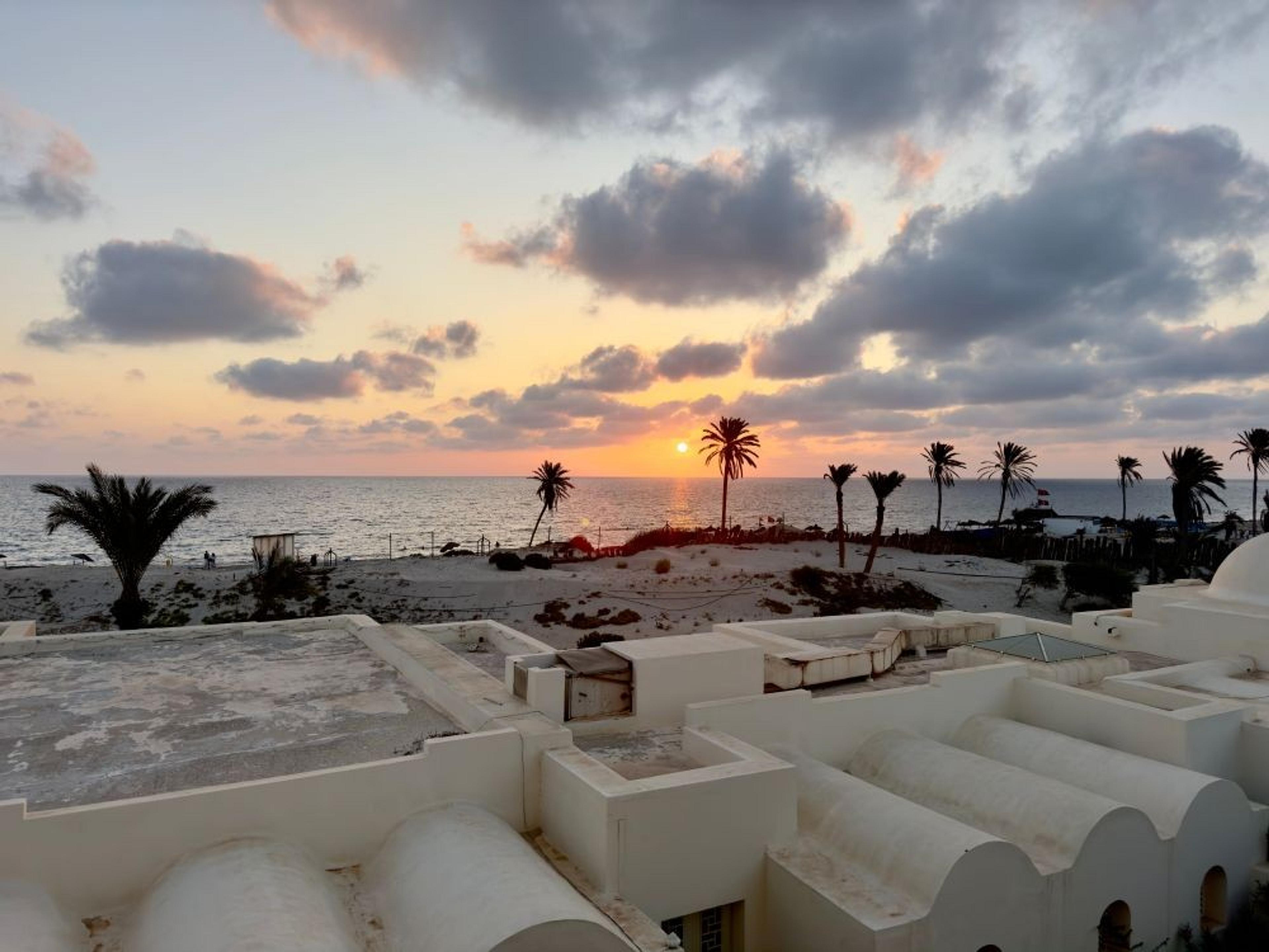 A stunning sunset over Djerba beach in Tunisia, with palm trees silhouetted against the colorful horizon.