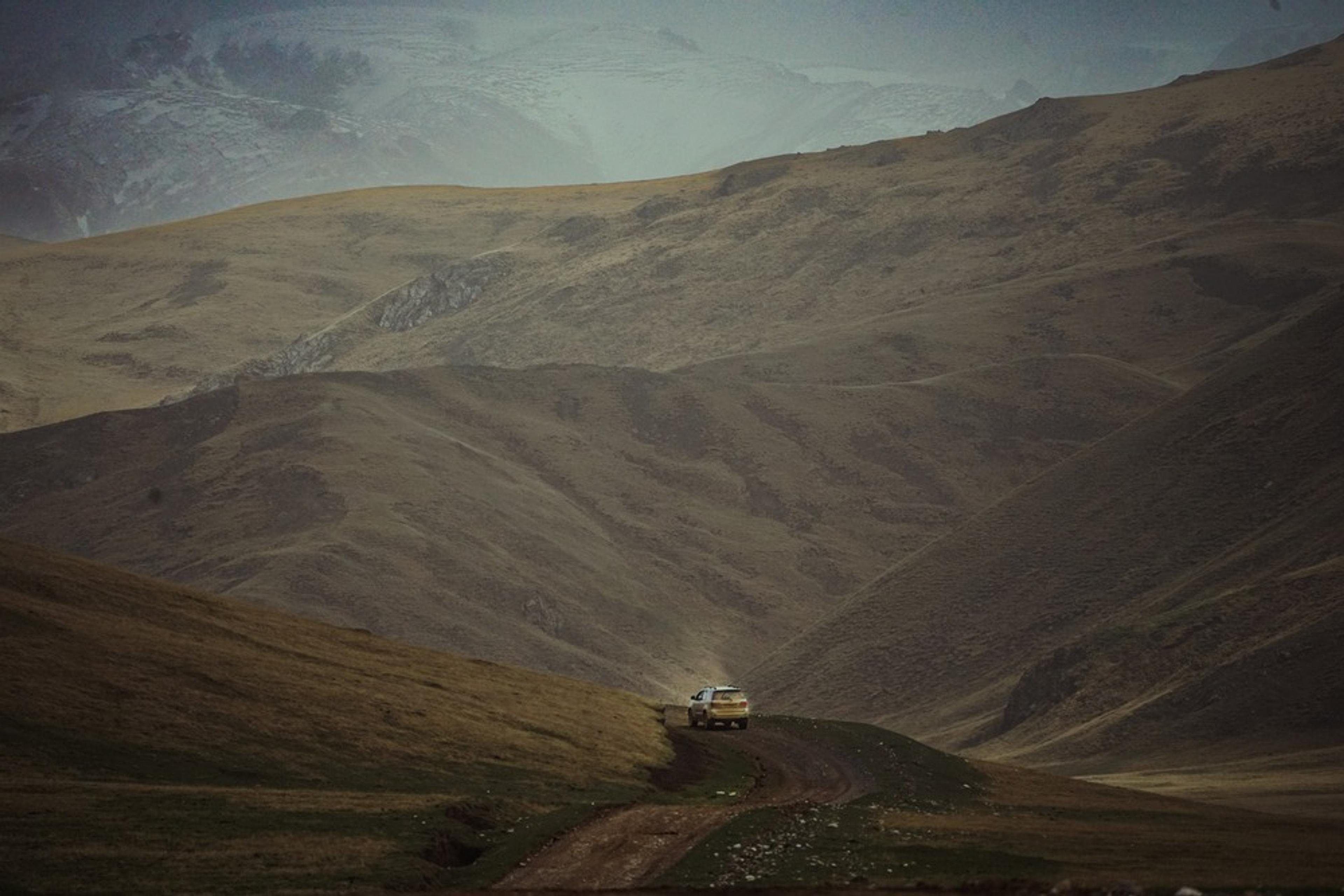 A lone car navigates a winding dirt road amidst the rolling hills of Kyrgyzstan.
