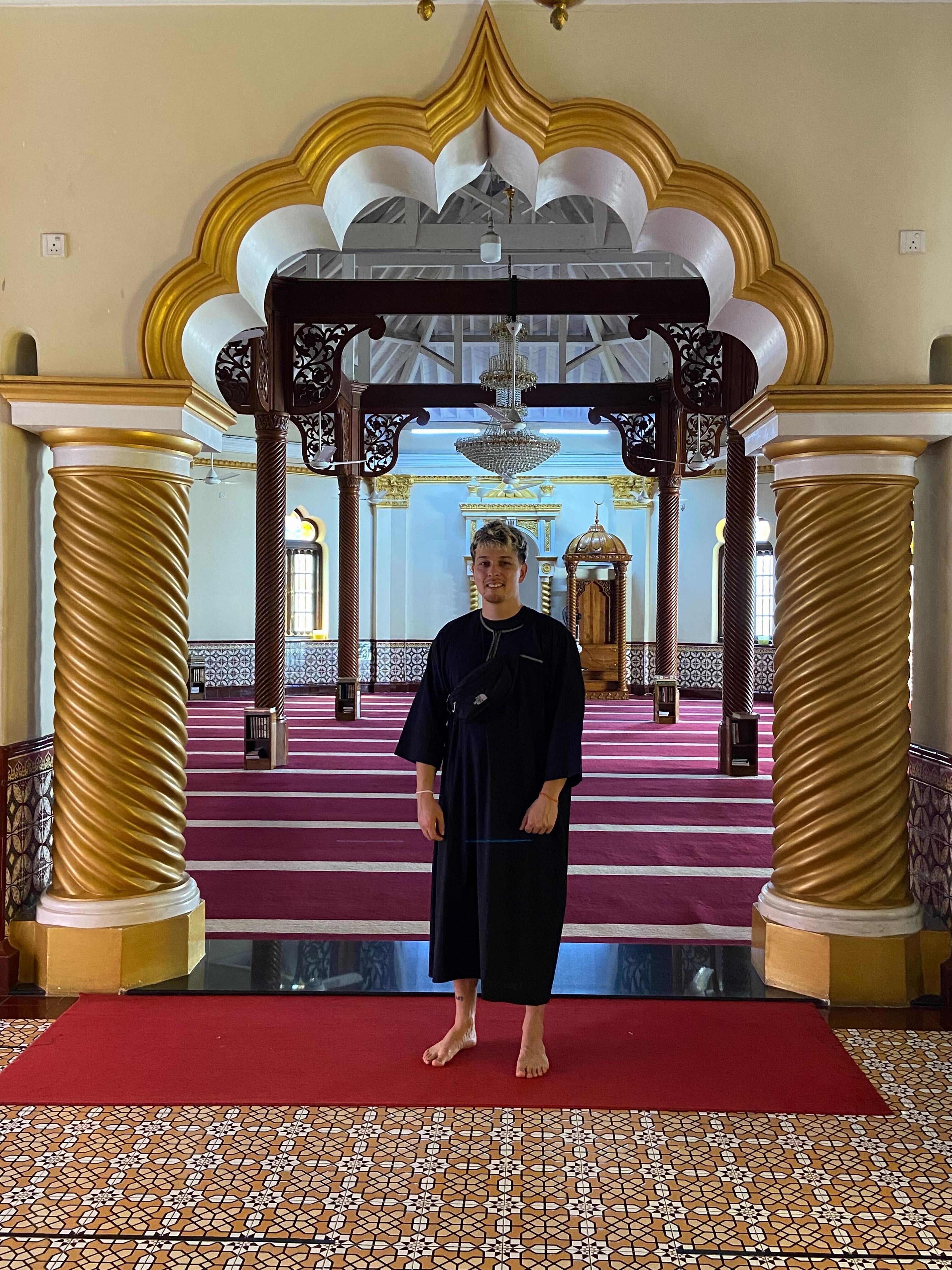 A person stands inside the Sultan Abu Bakar State Mosque in Johor Bahru, Malaysia, surrounded by ornate arches and a richly patterned interior.