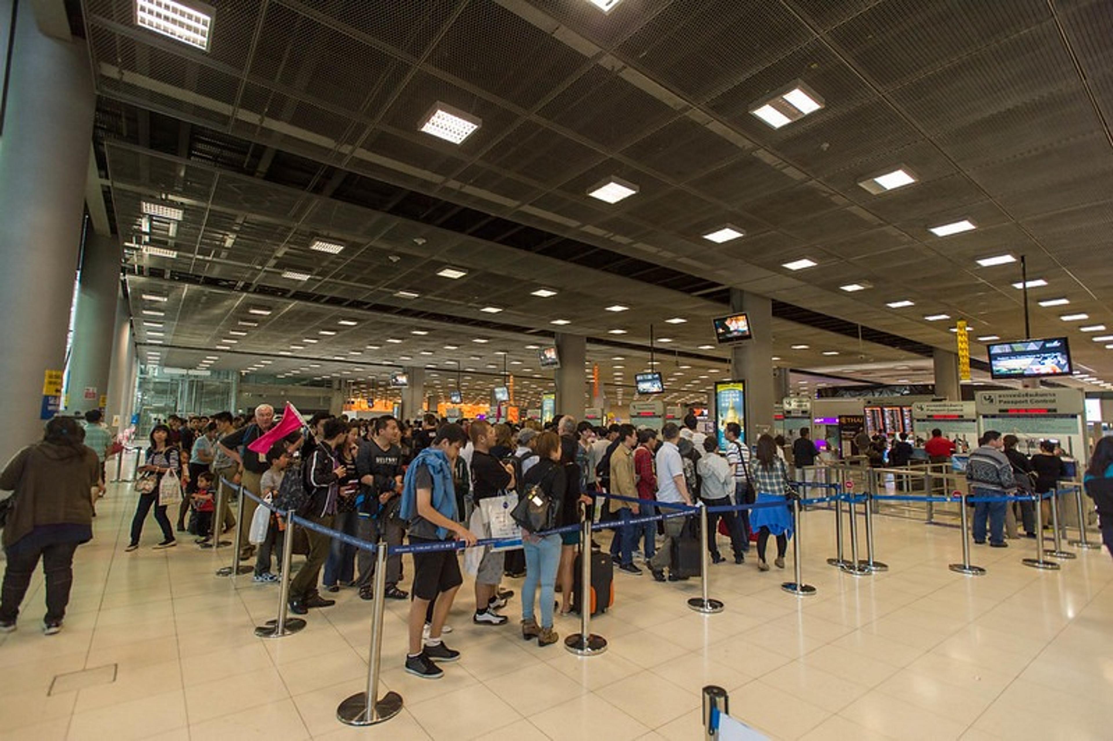 Travelers queue at Dubai International Airport, surrounded by check-in counters and overhead screens.