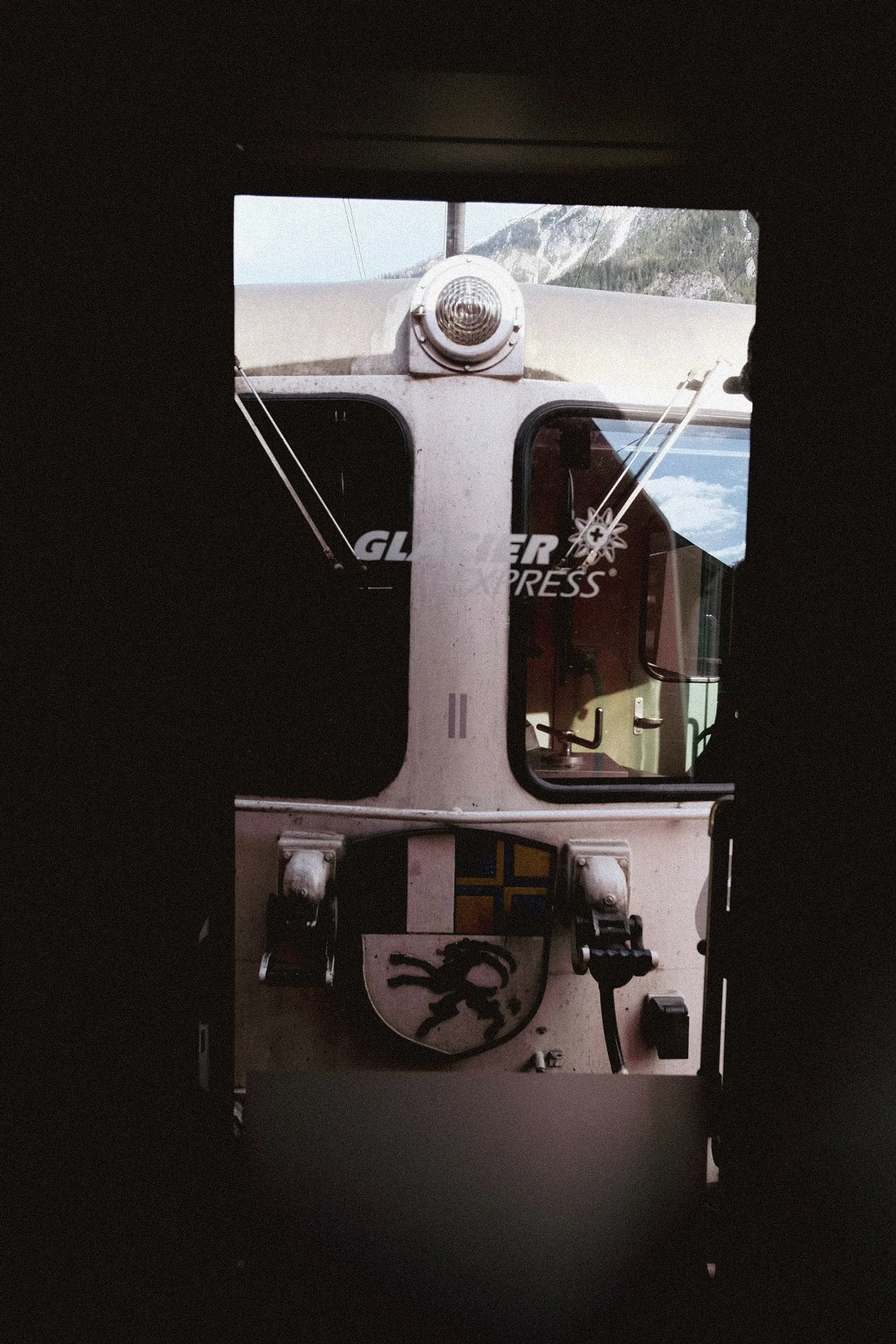 The iconic Glacier Express train is framed through a dark doorway, set against the backdrop of the Swiss Alps.