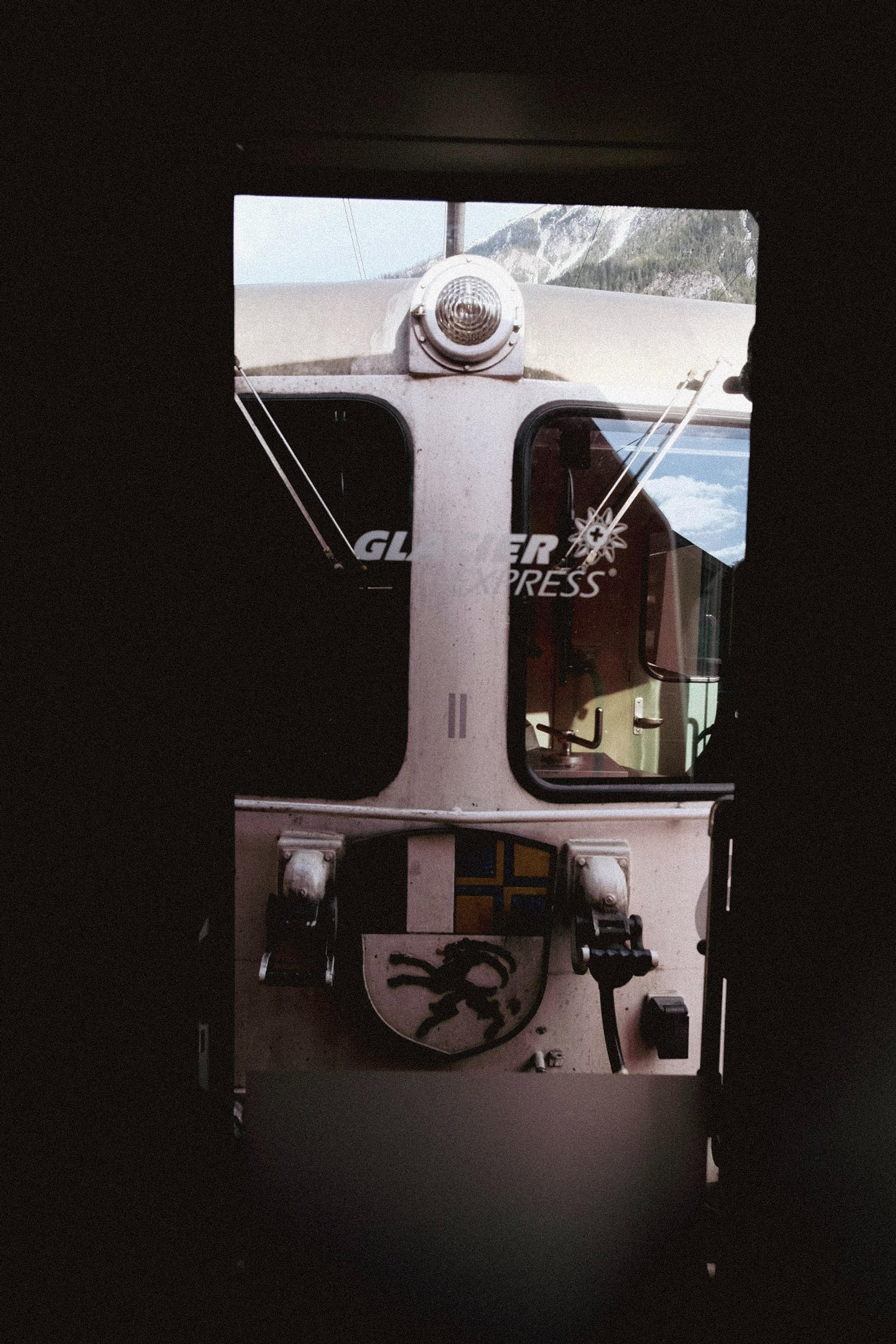 The iconic Glacier Express train is framed through a dark doorway, set against the backdrop of the Swiss Alps.
