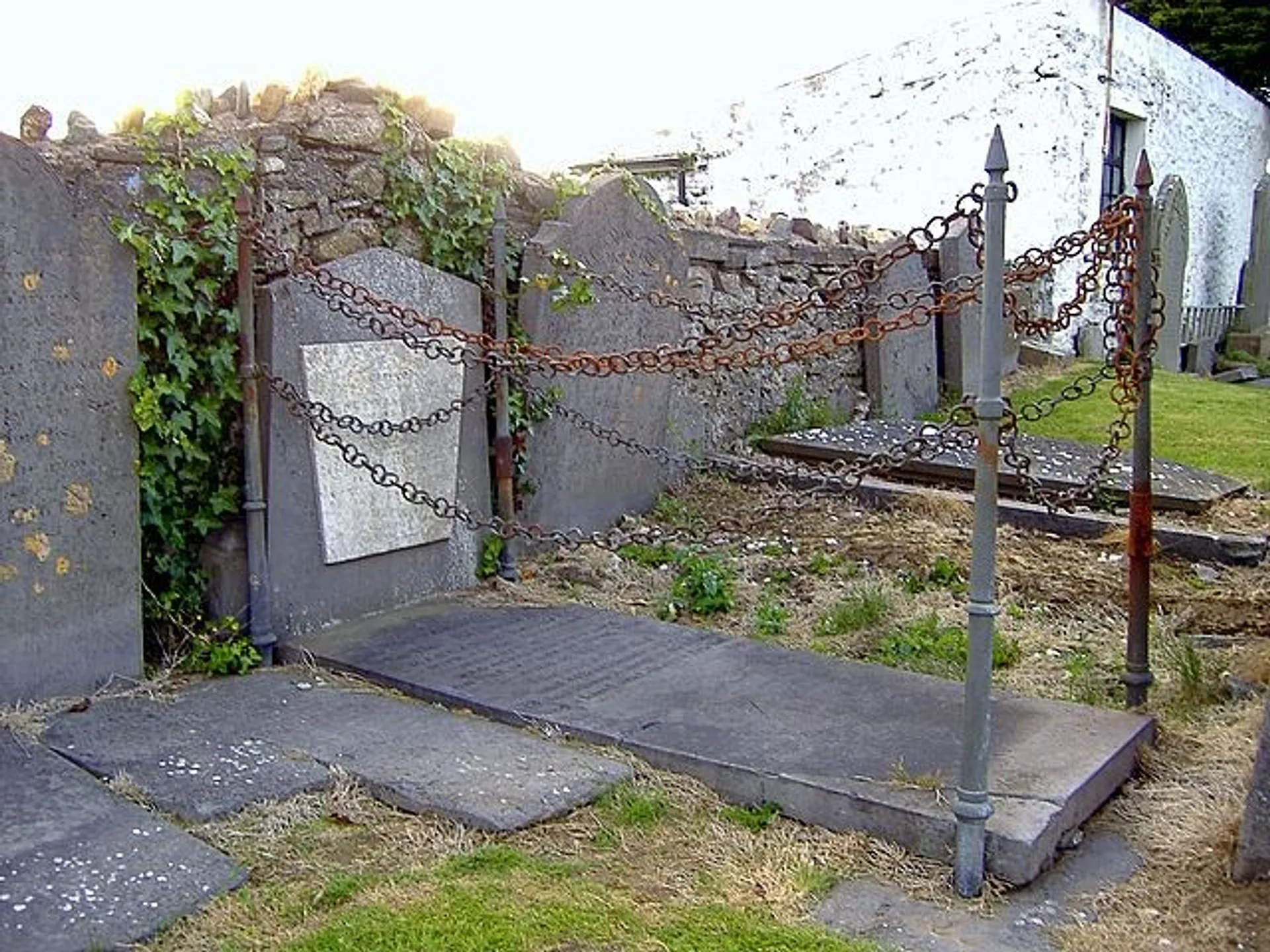 A historic grave with an iron chain fence is set against a stone wall