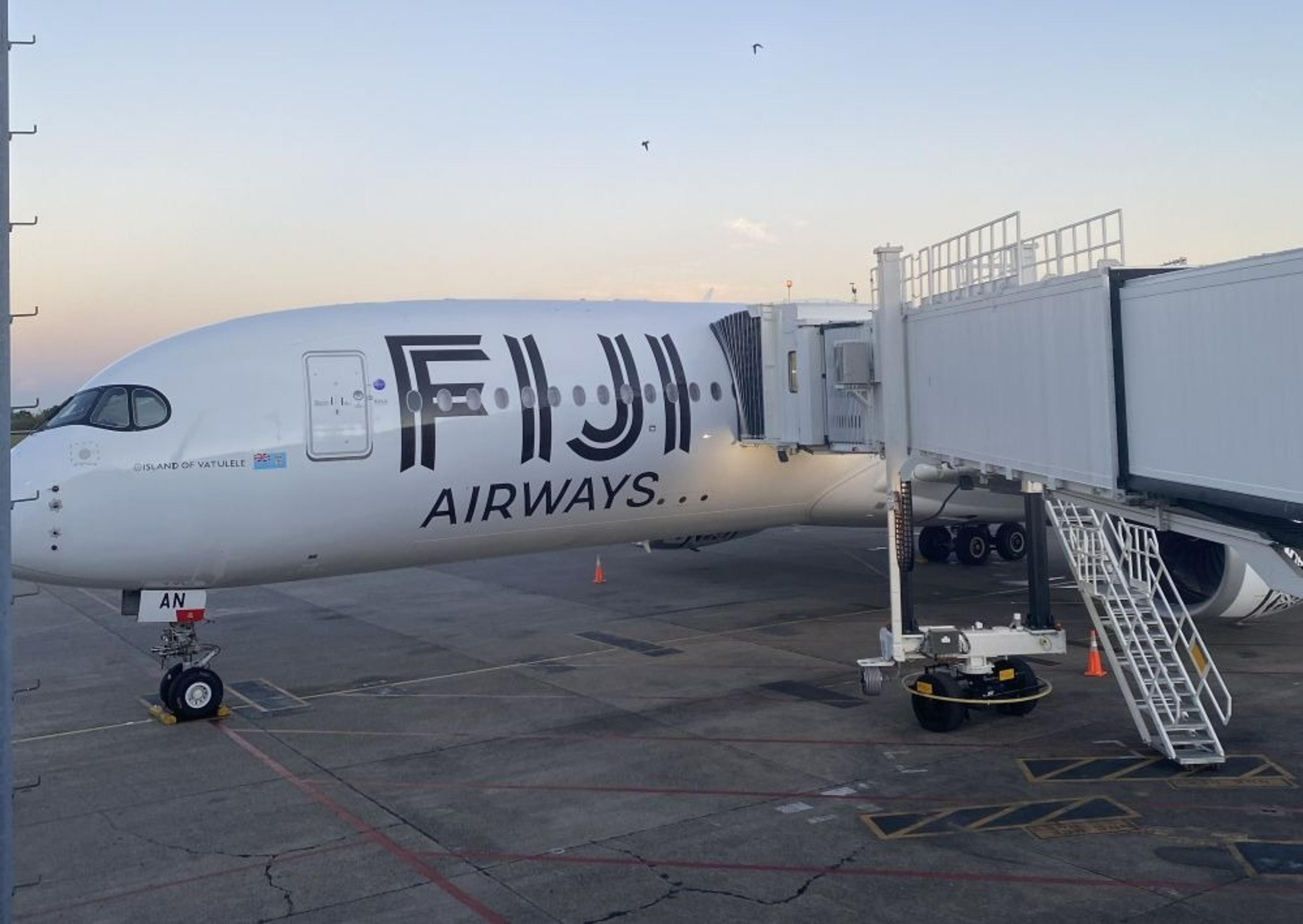 A Fiji Airways airplane is parked at a jet bridge, likely at Nadi International Airport.