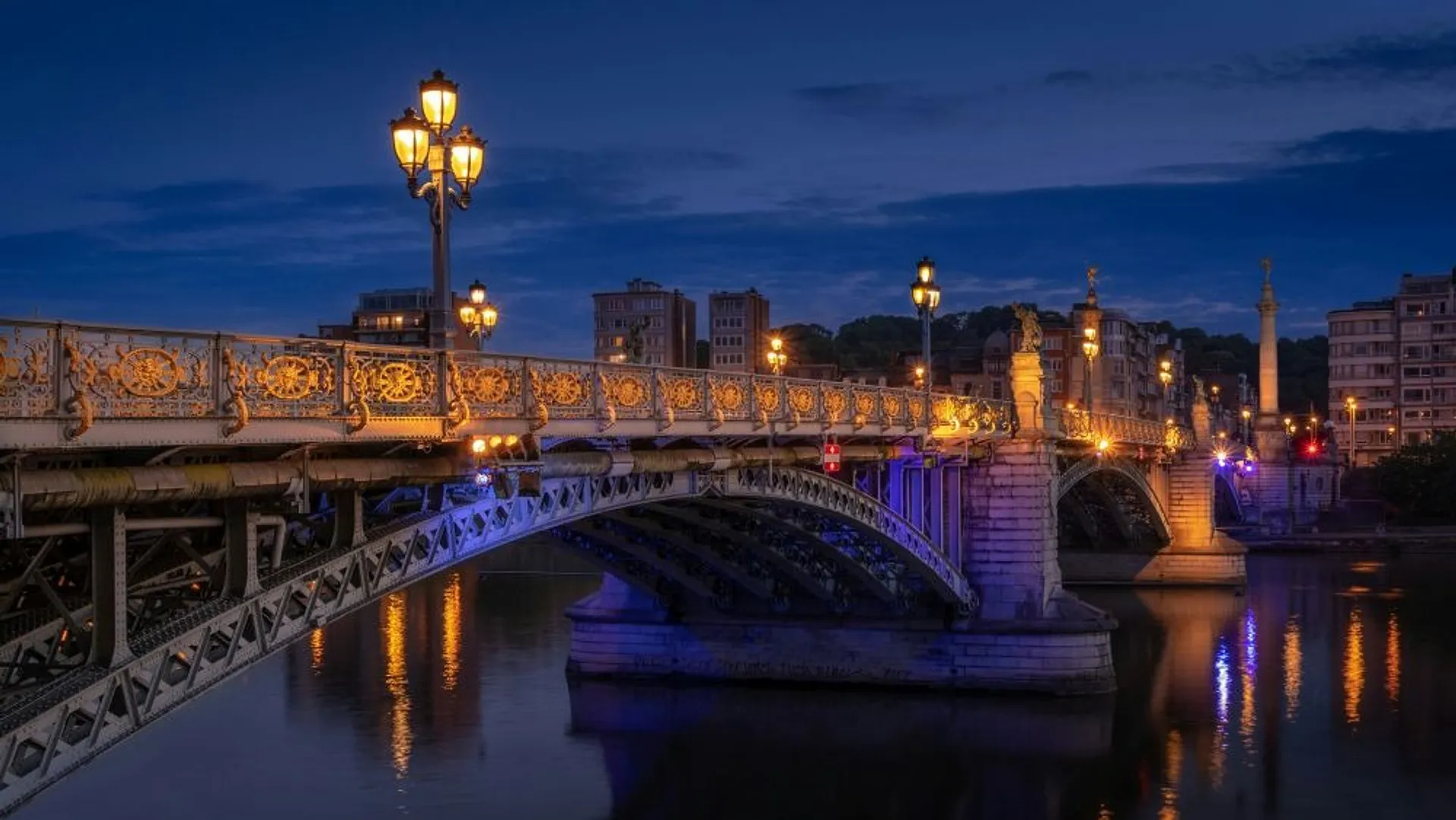 Bridge in Liege illuminated at dusk, reflecting in the calm river below.
