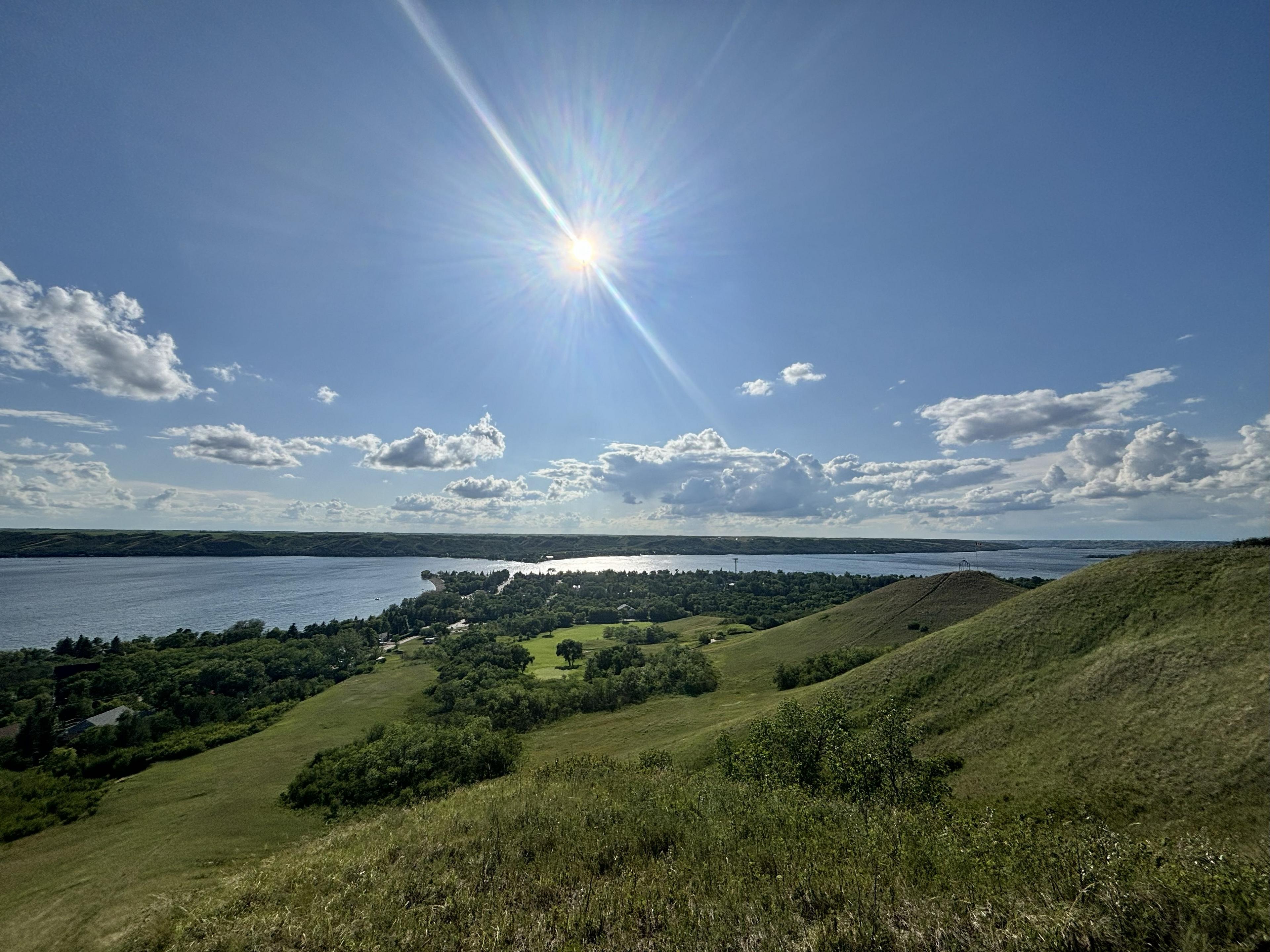The Qu'Appelle Valley in Saskatchewan displays rolling hills and a reflective river under a bright sun.