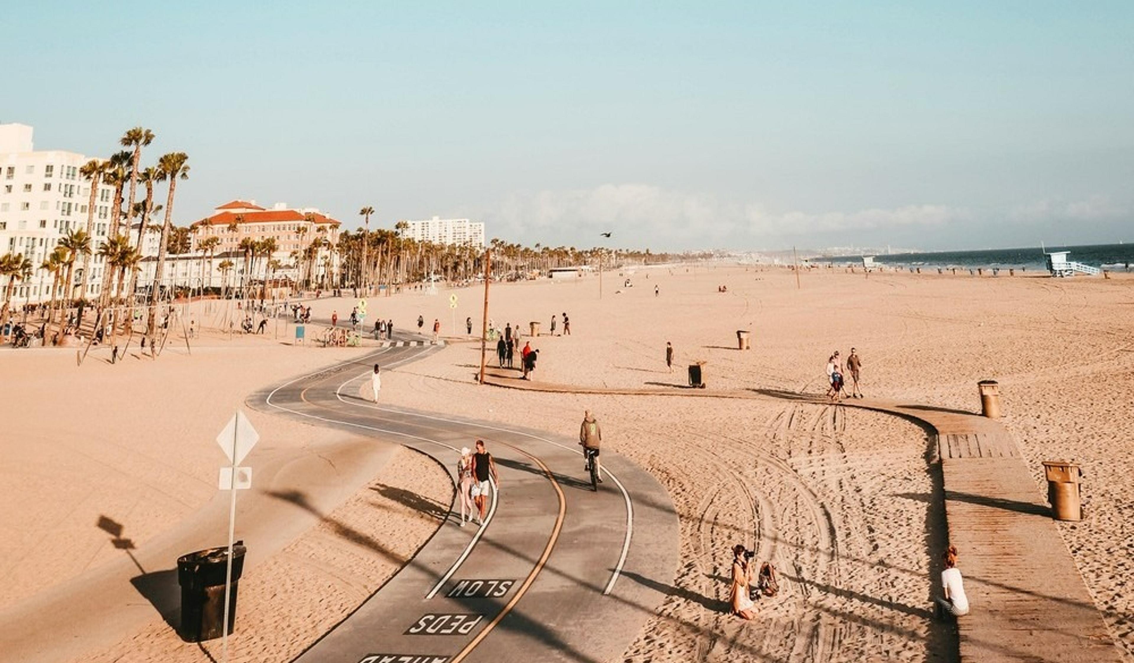 A sunny day unfolds on Santa Monica Beach in California, featuring palm-lined pathways and distant ocean views.