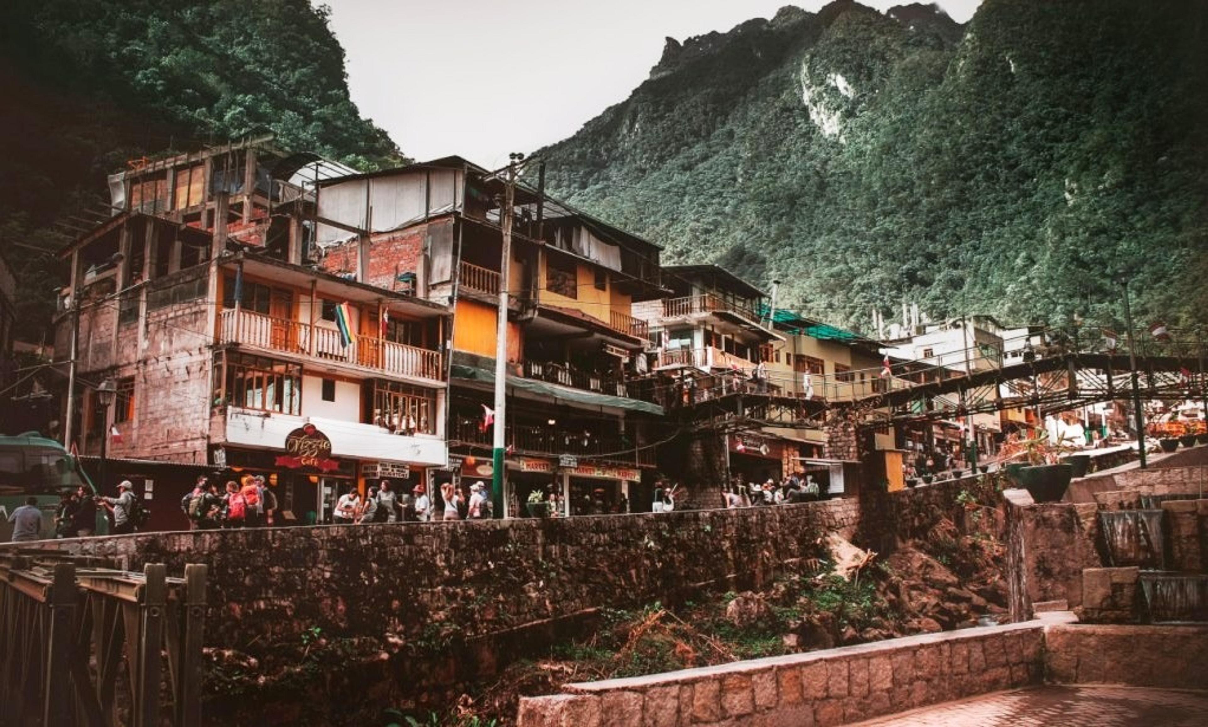 A bustling street scene unfolds in the town of Aguas Calientes, Peru, nestled among verdant mountains.