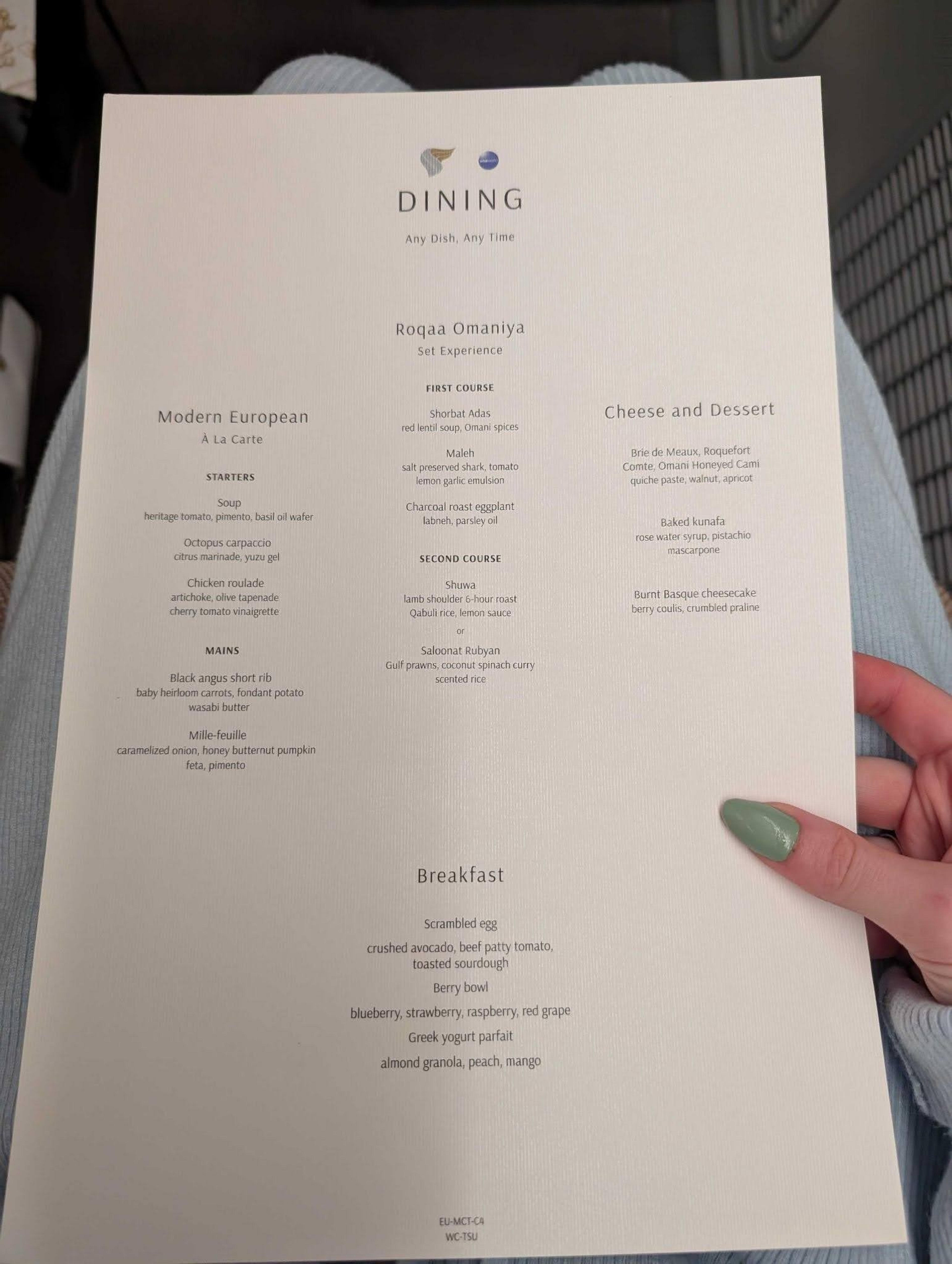 A dining menu from Oman Air featuring diverse culinary options is held on an airplane seat.