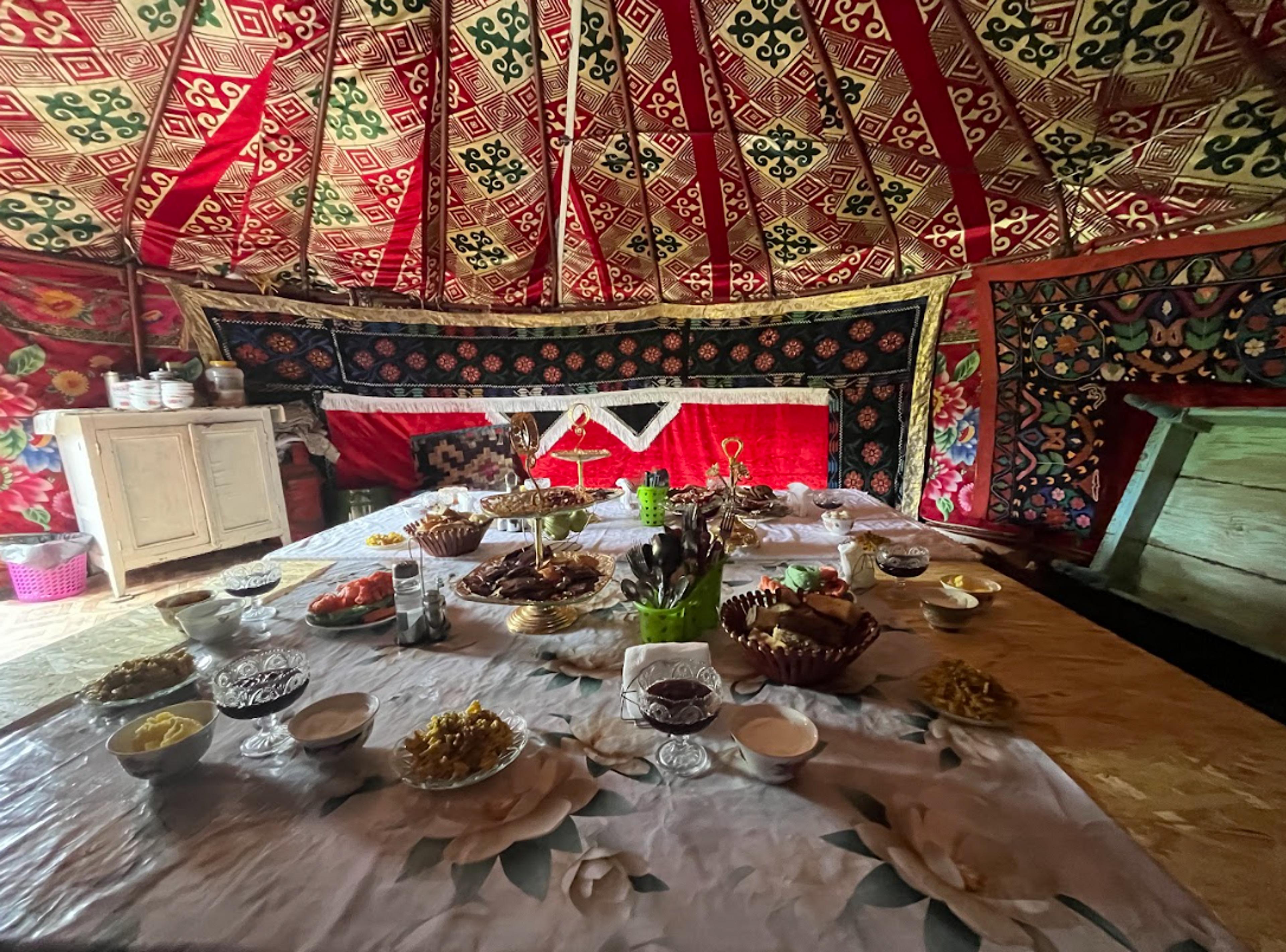 A richly decorated yurt interior in Central Asia features a table set with an array of traditional foods.