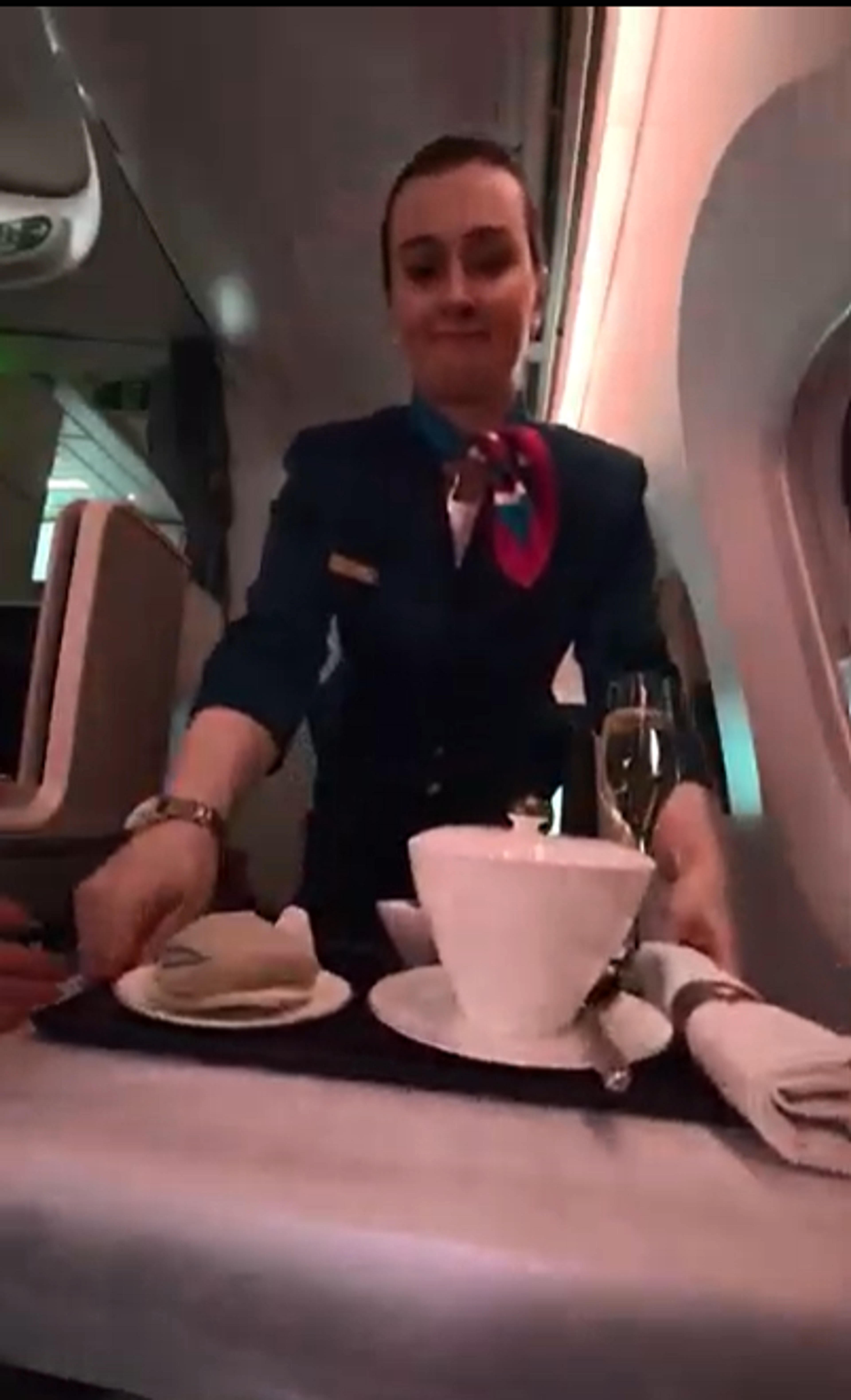 A flight attendant serves a meal in the business class section of an airplane.