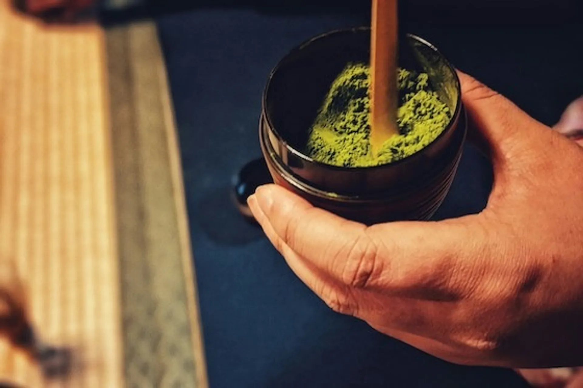 A hand prepares matcha tea in a traditional Japanese setting.