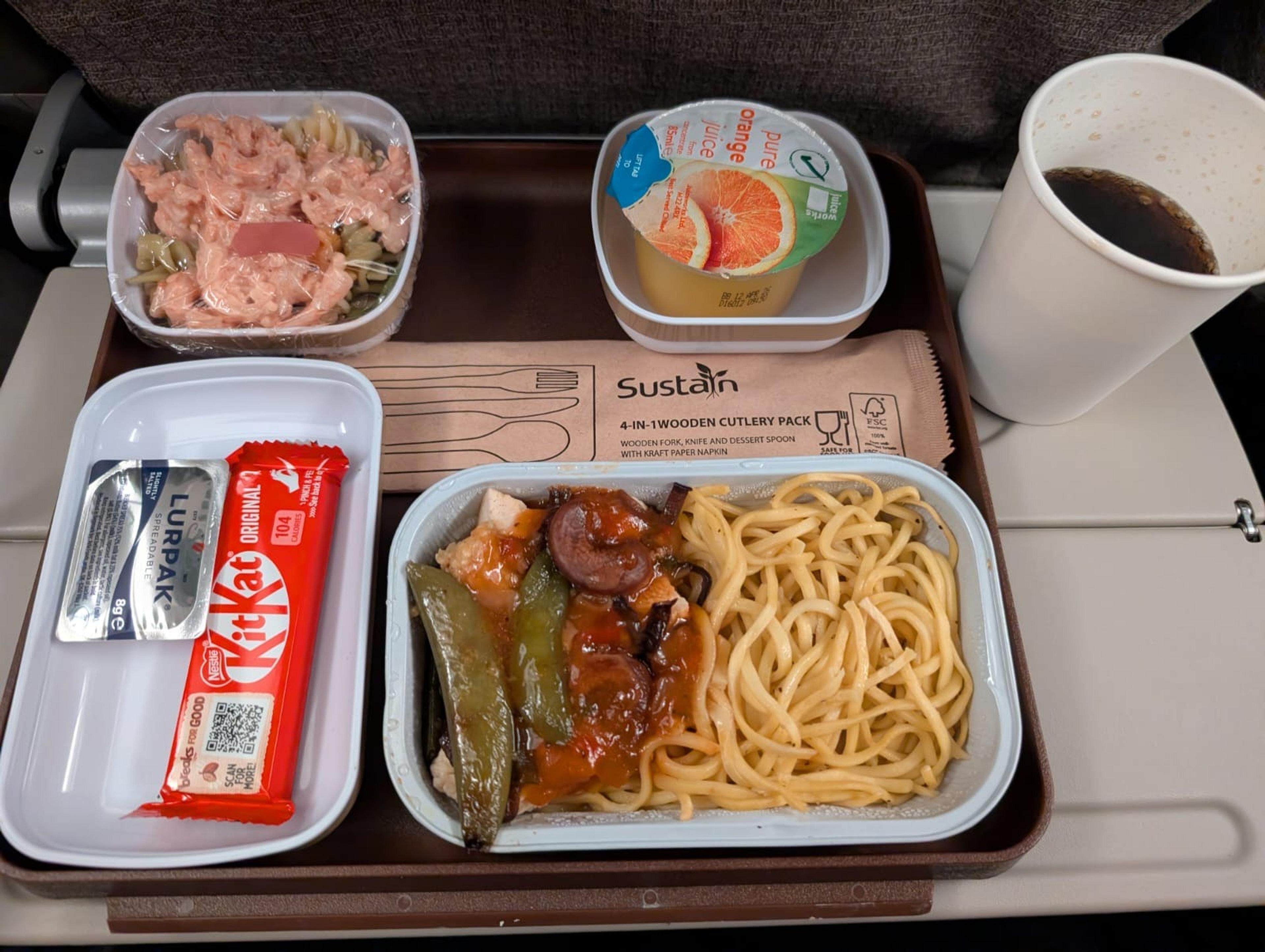 A meal tray from China Eastern Airlines features pasta, salad, orange juice, a KitKat, and a cup of soda.