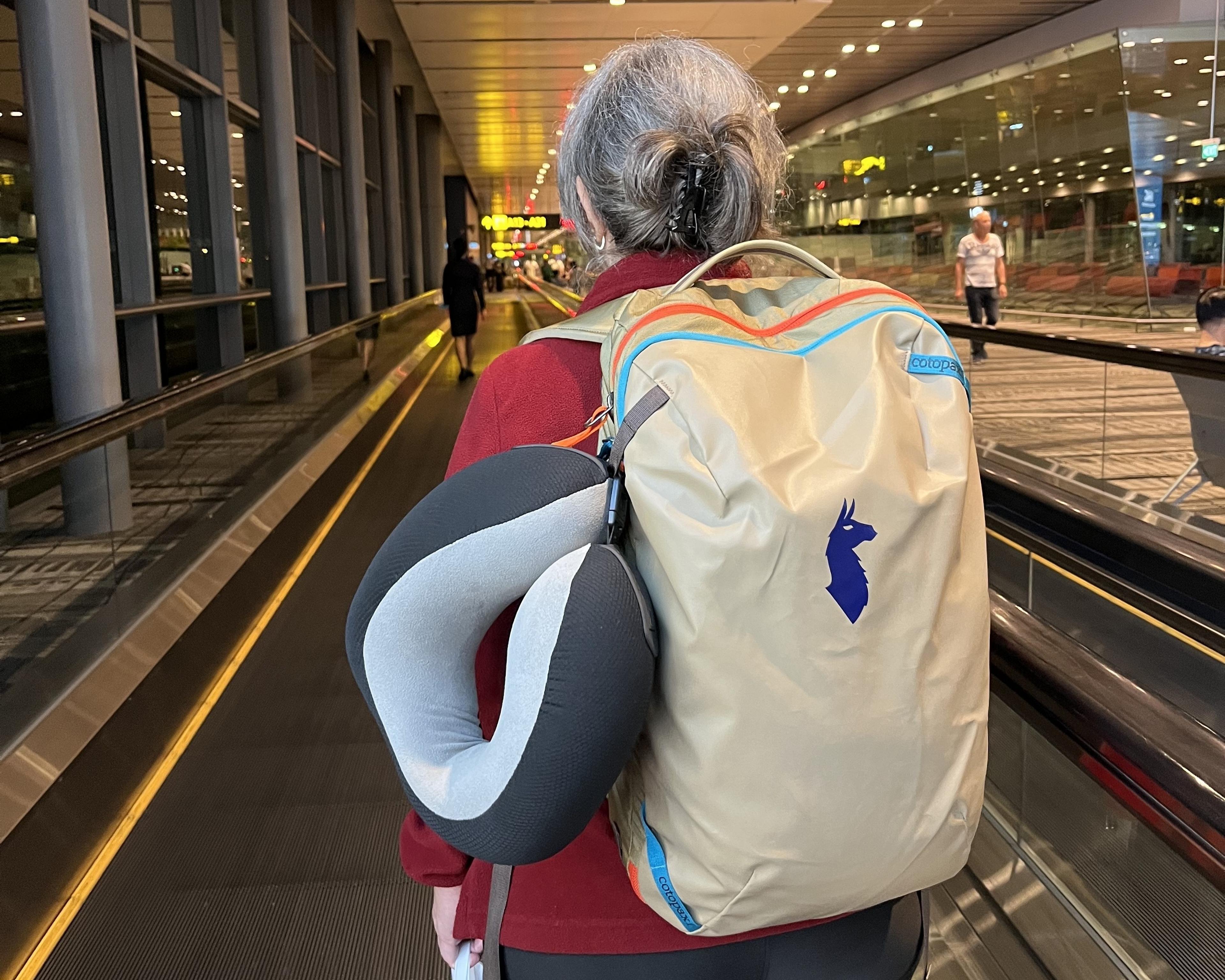 A traveler with a beige Cotopaxi backpack moves through Changi Airport's terminal in Singapore.
