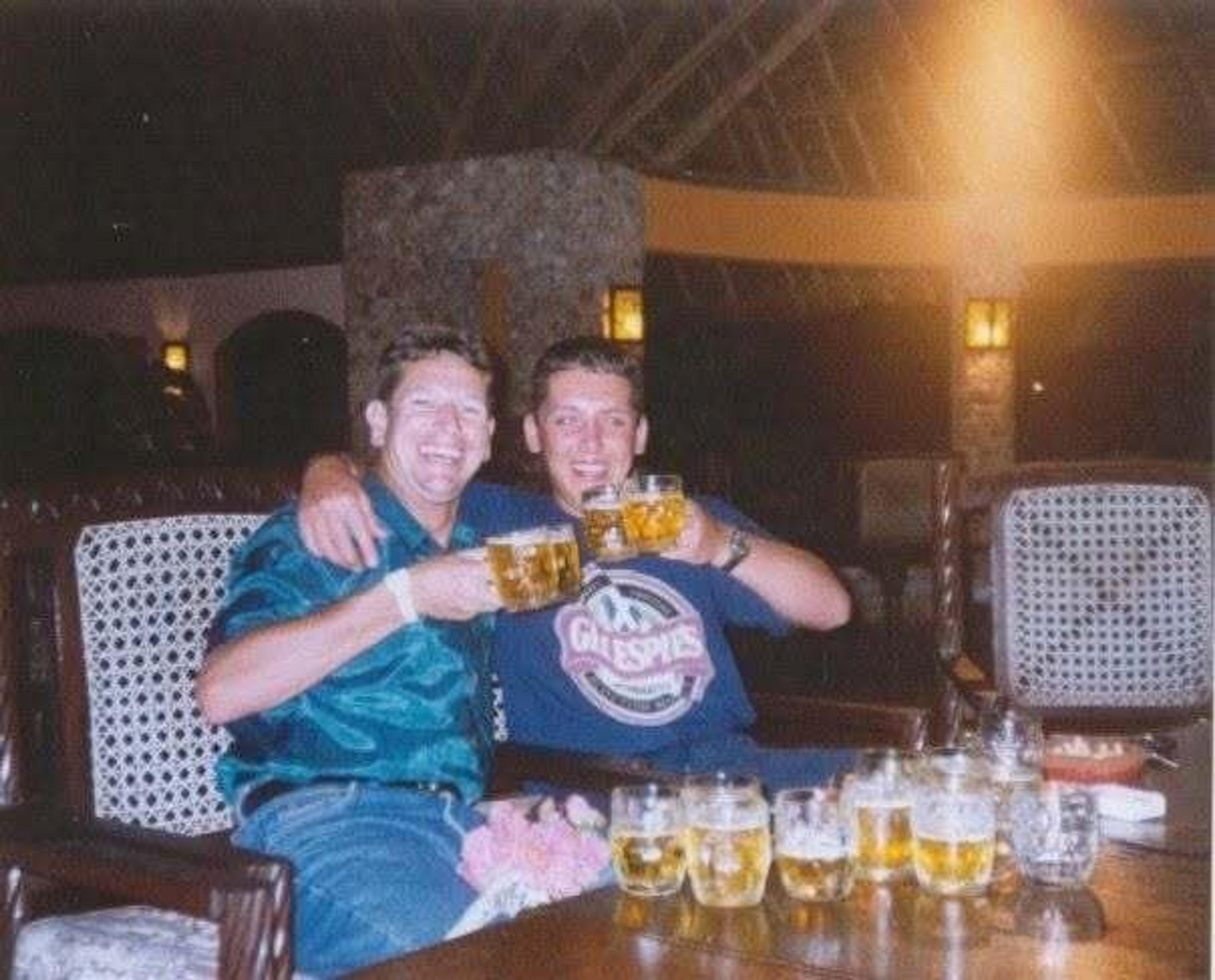 Two people enjoying beers in a cozy lounge setting with wicker chairs and ambient lighting, possibly at a resort.