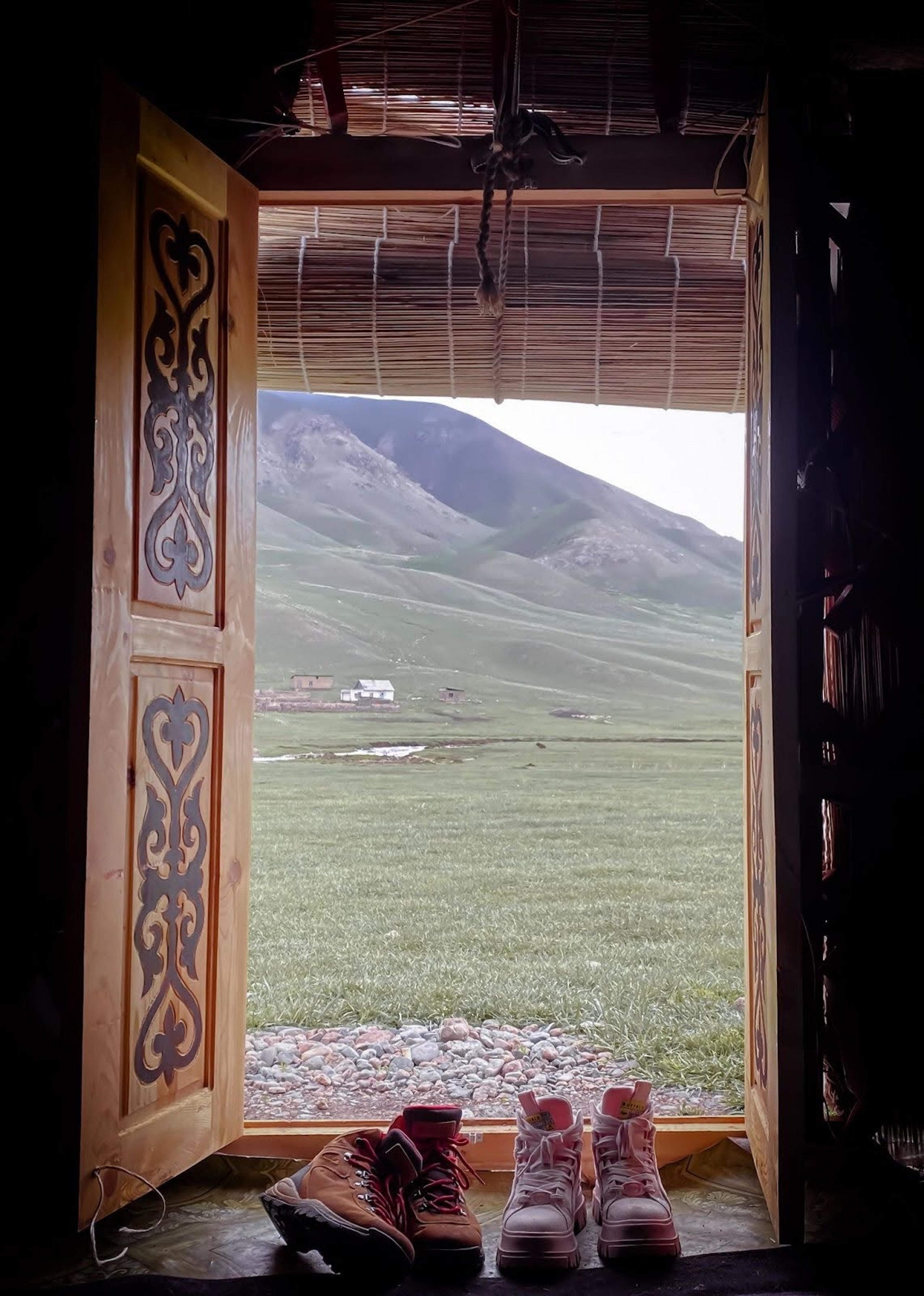 A traditional Kyrgyz yurt with an open door revealing a grassy landscape and distant mountains.