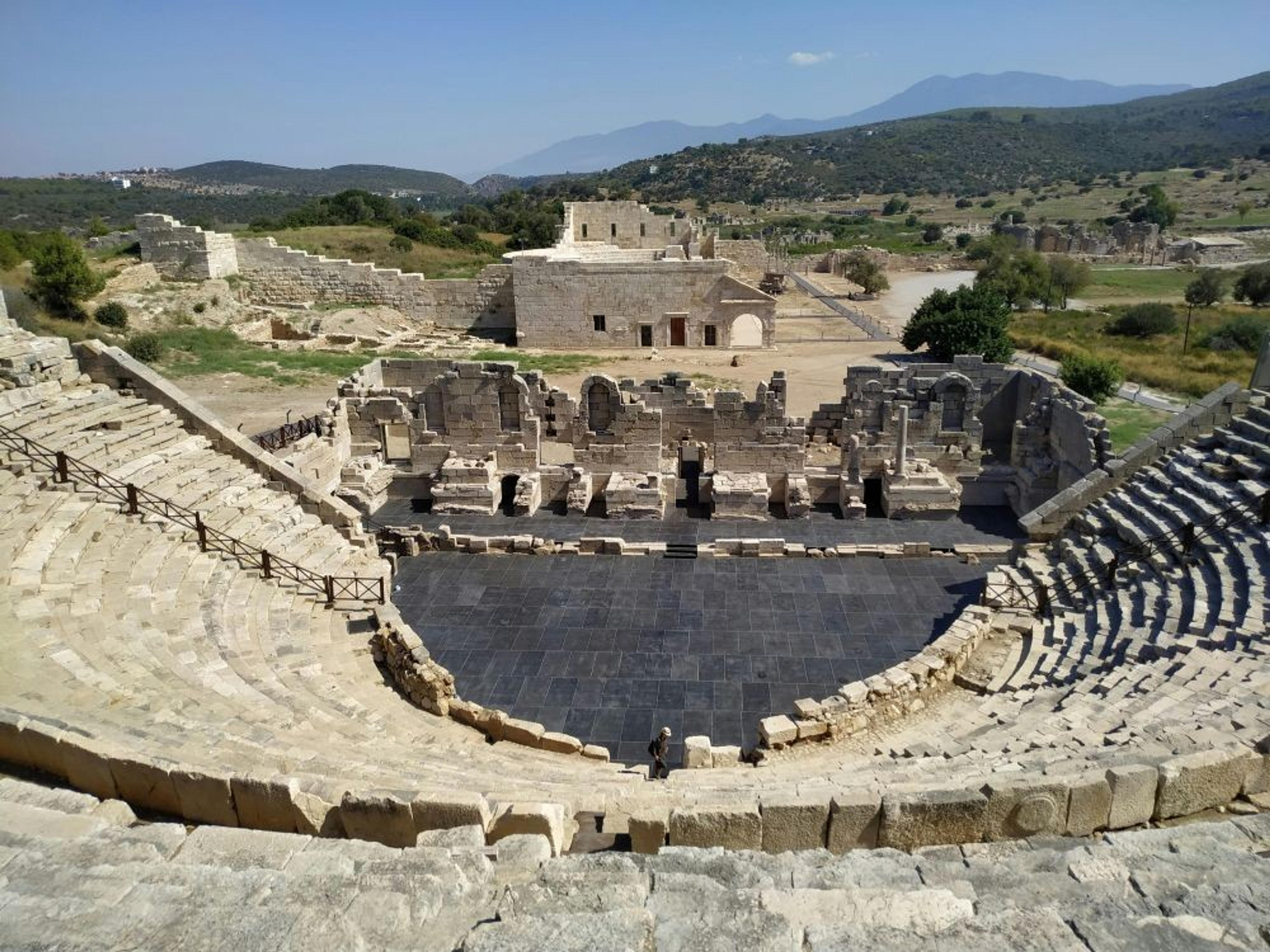 An ancient amphitheater in Patara, Turkey, stands amidst a landscape of ruins and distant mountains.