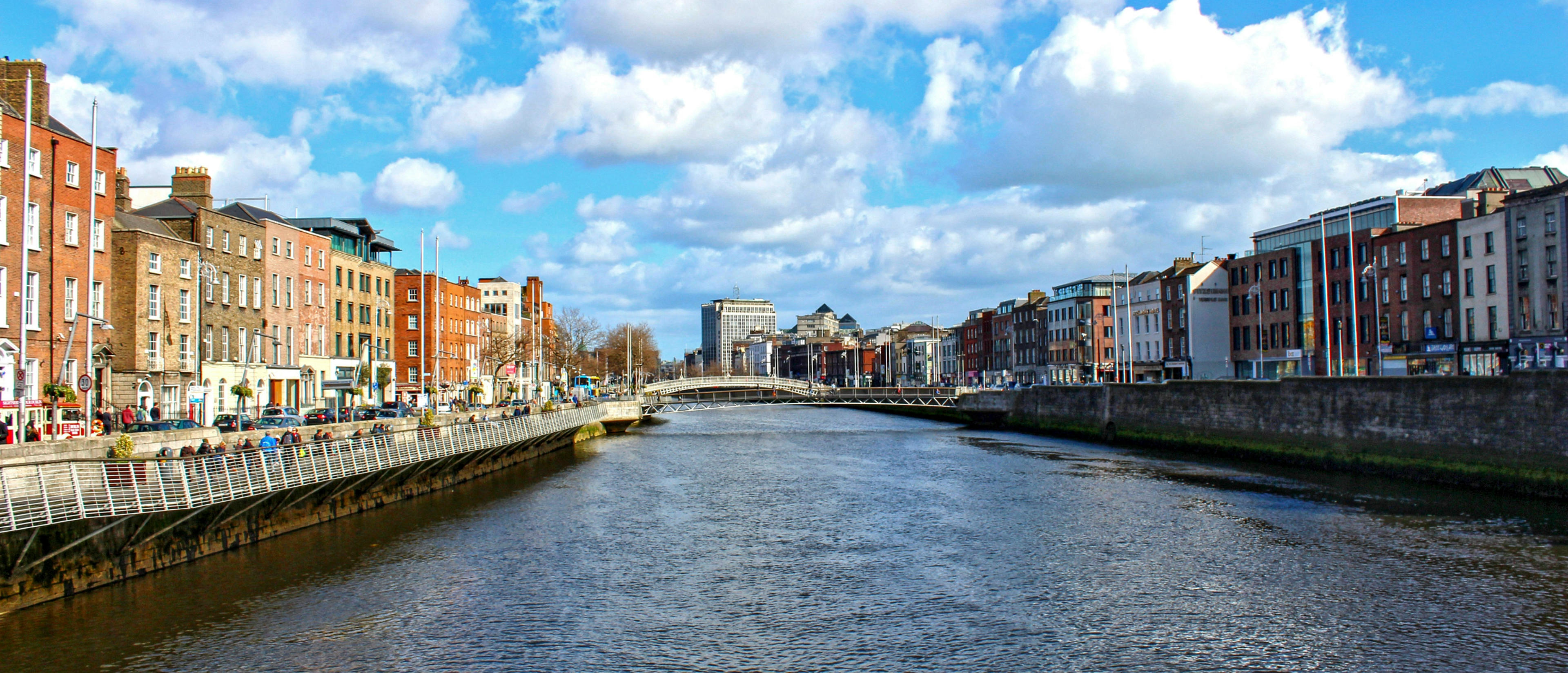 Historic buildings line the banks of the River Liffey in Dublin, Ireland, under a sky dotted with clouds.