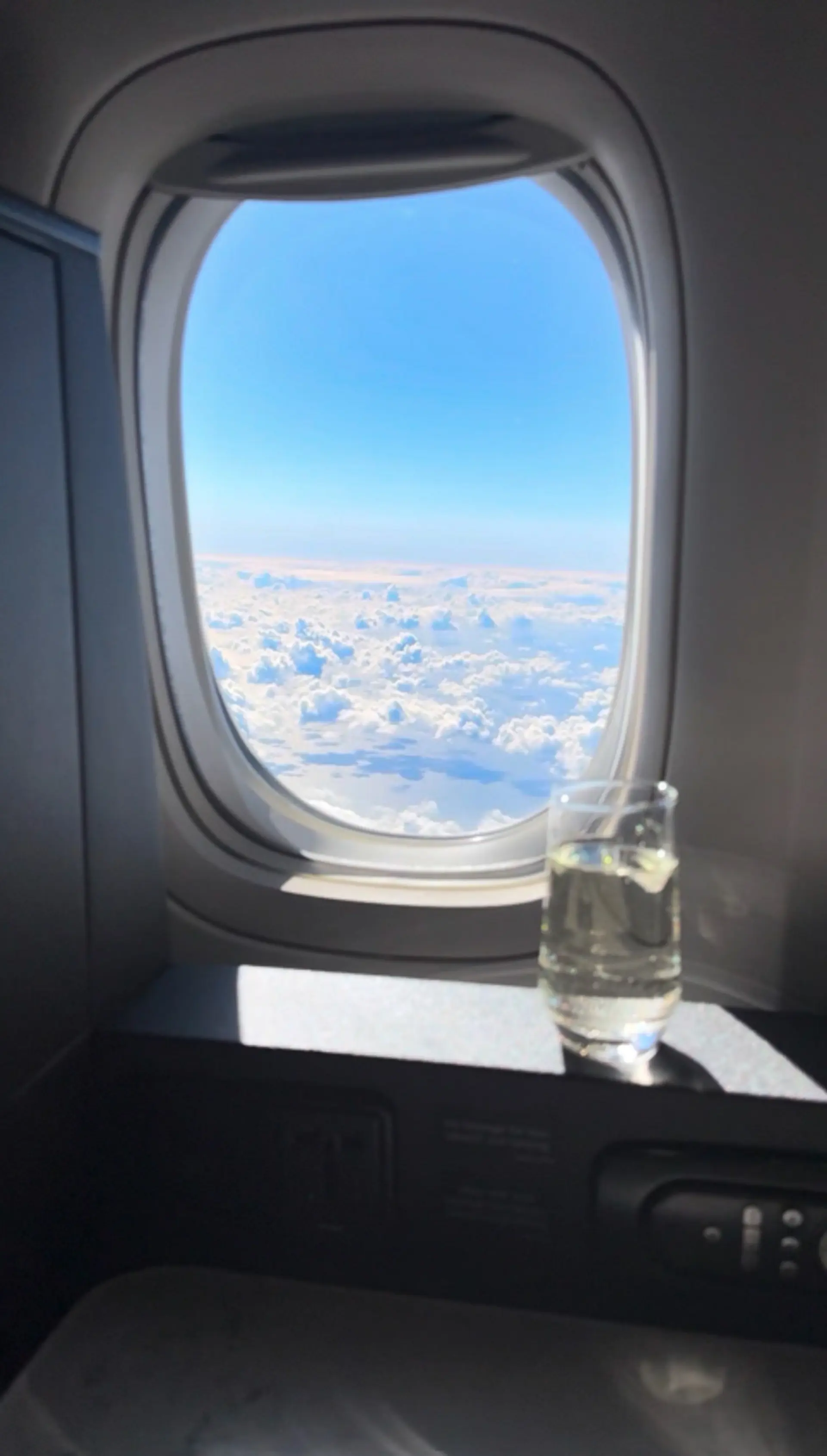 A view of fluffy white clouds from an airplane window with a glass of water on the ledge.