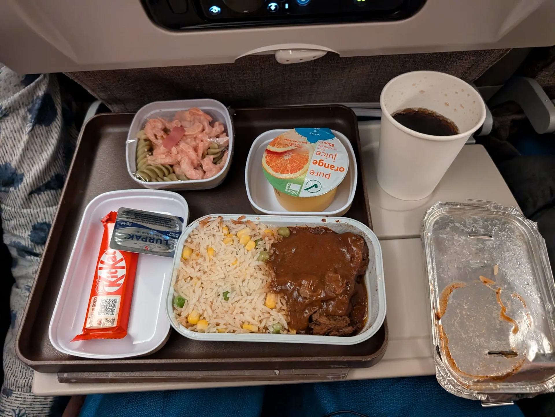 A China Eastern Airlines meal tray features beef with rice and vegetables, pasta salad, a Kit Kat bar, orange juice, and coffee.