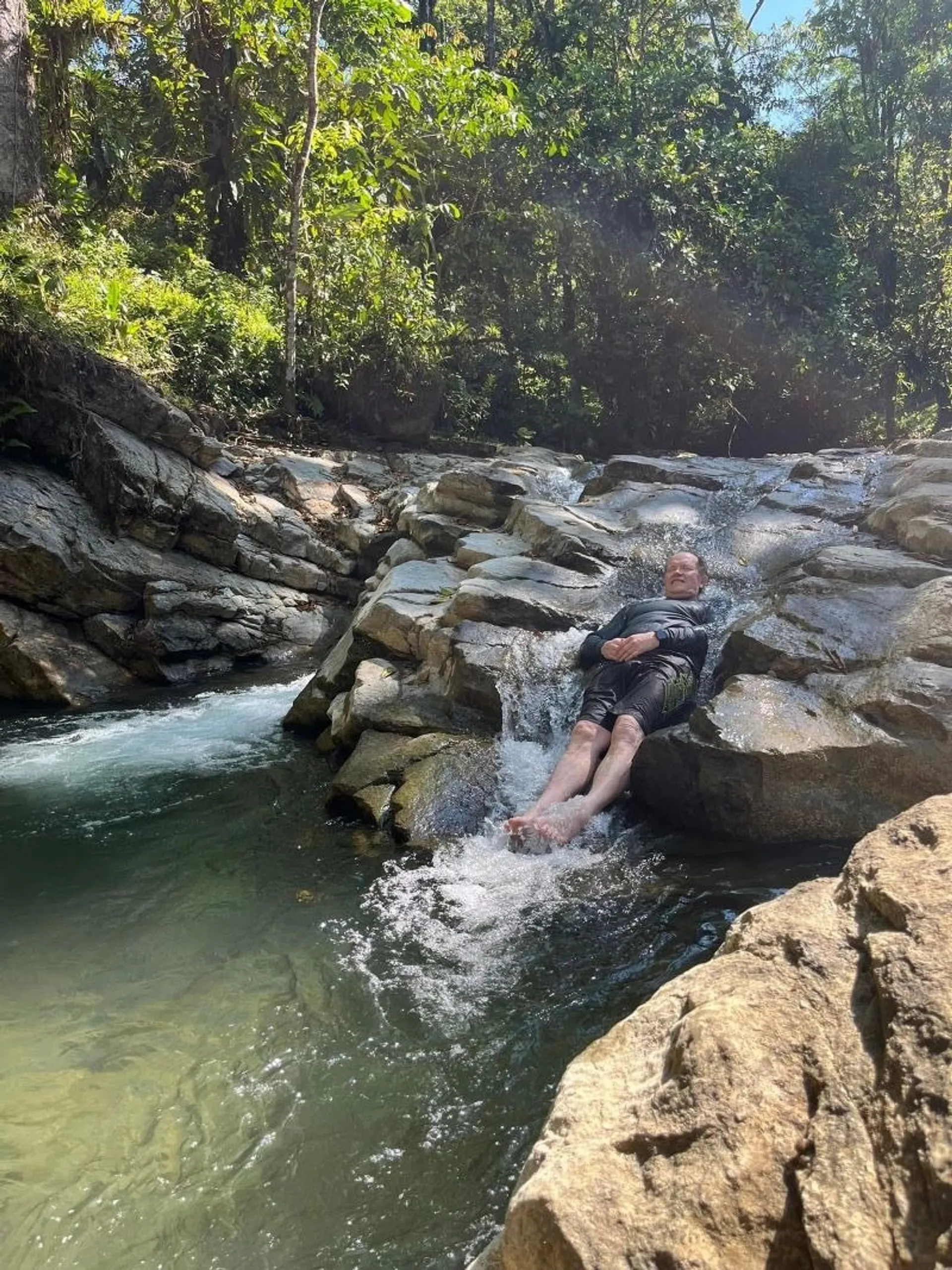 A person slides down a rocky stream within a lush forest in Costa Rica.