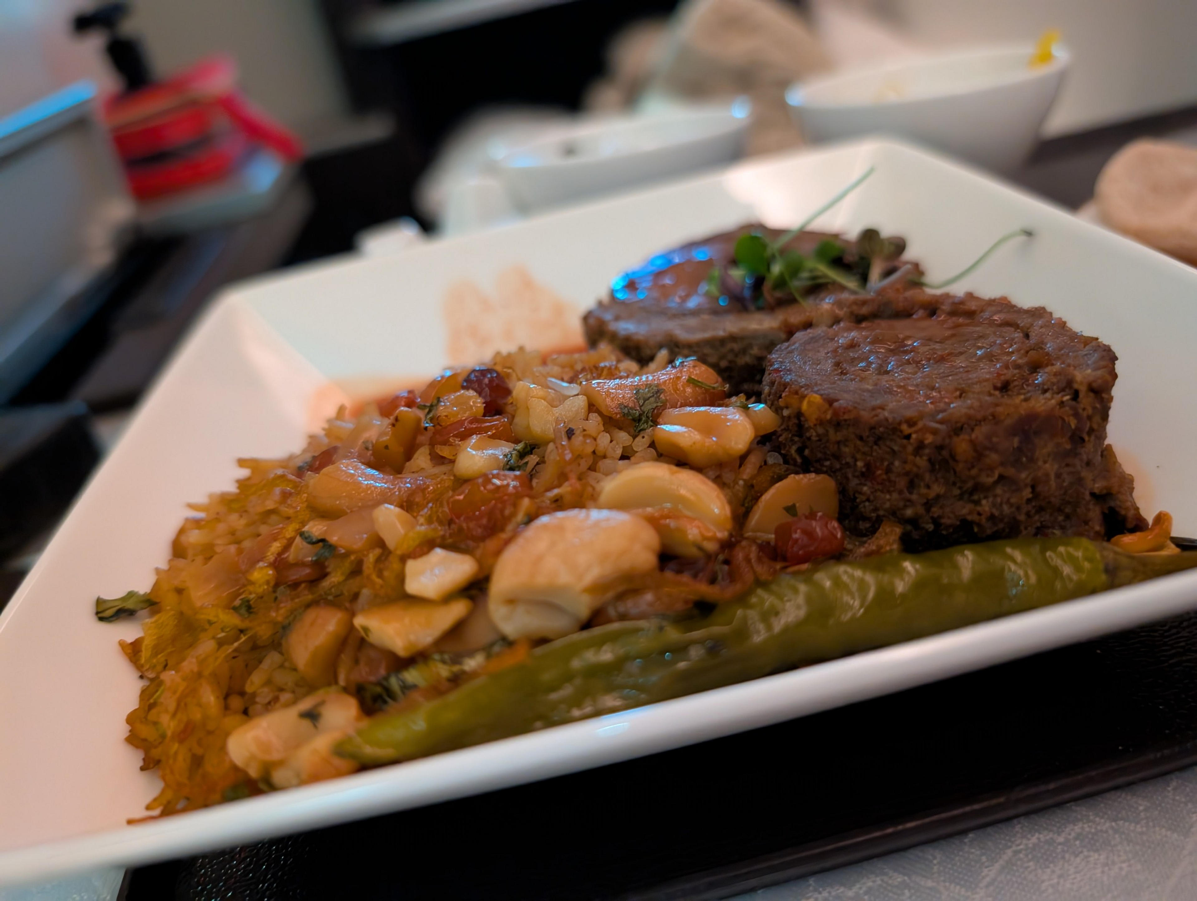 A delicious Middle Eastern-inspired dish featuring flavorful rice with nuts, garnished with stuffed vine leaves and accompanied by savory meat slices in an elegant dining setting.