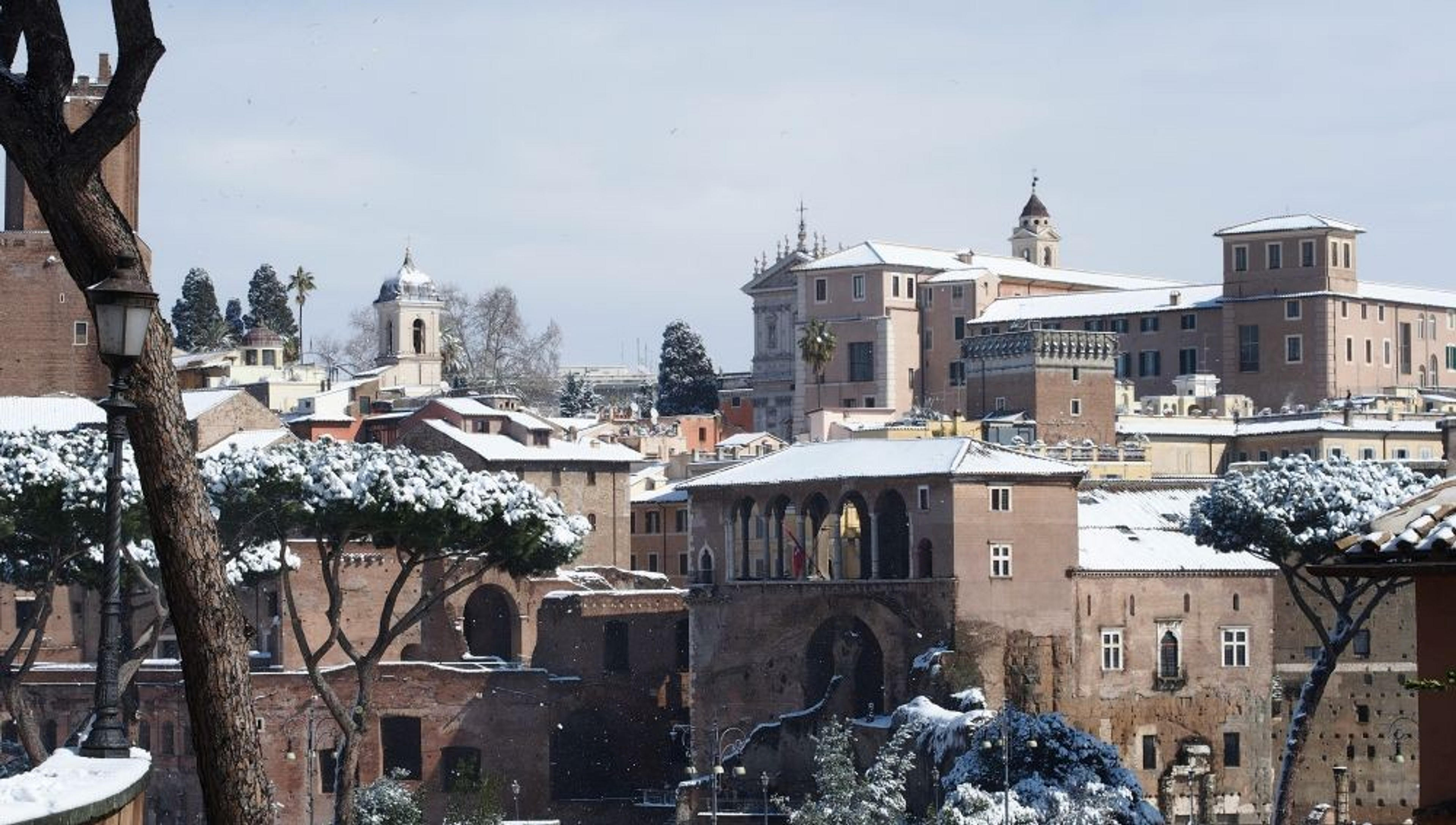 A snowy winter scene blankets the historical architecture of Rome, Italy, highlighting its iconic trees and ancient buildings.