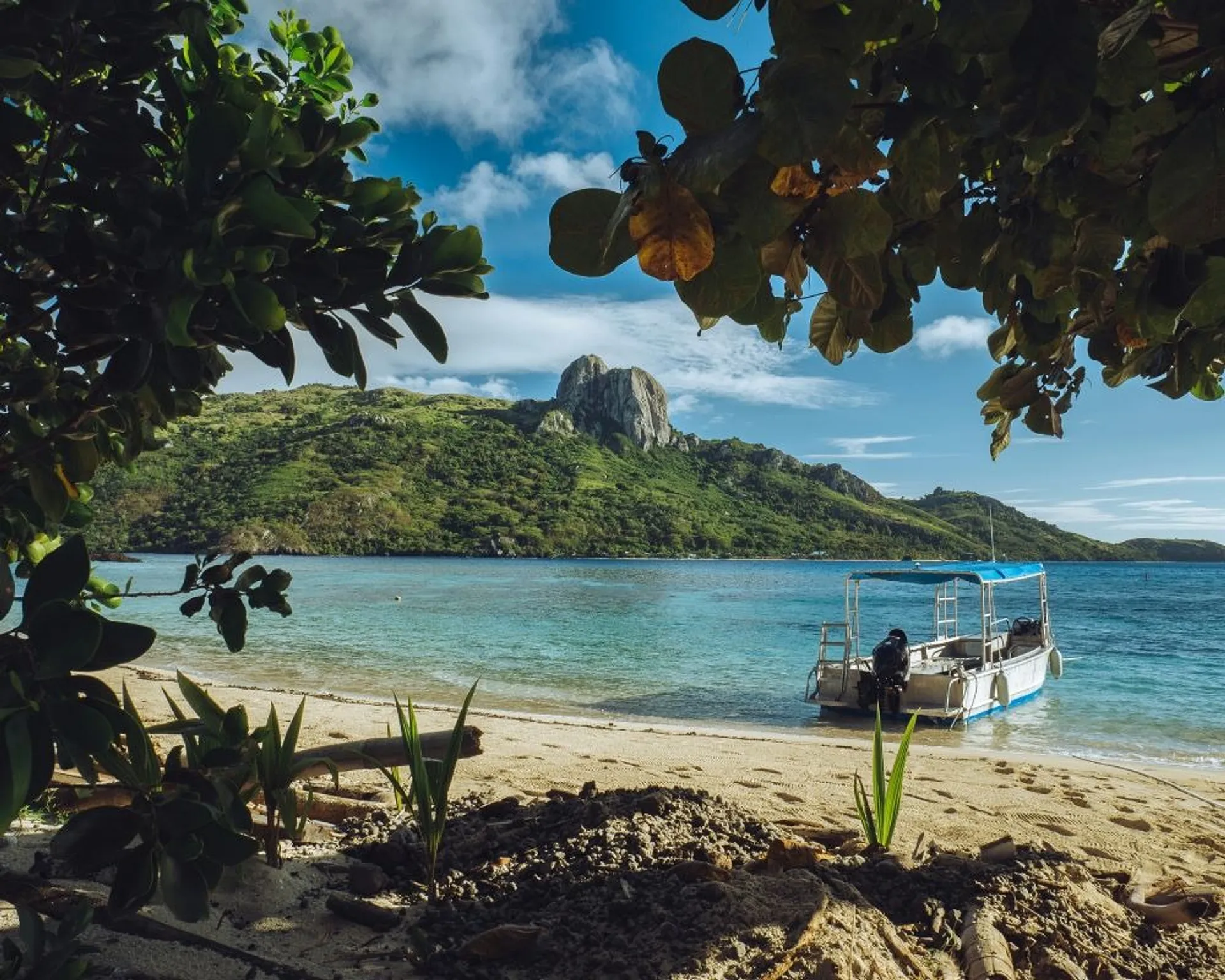 Secluded, leafy beach with a small boat floating by the shore, Fiji