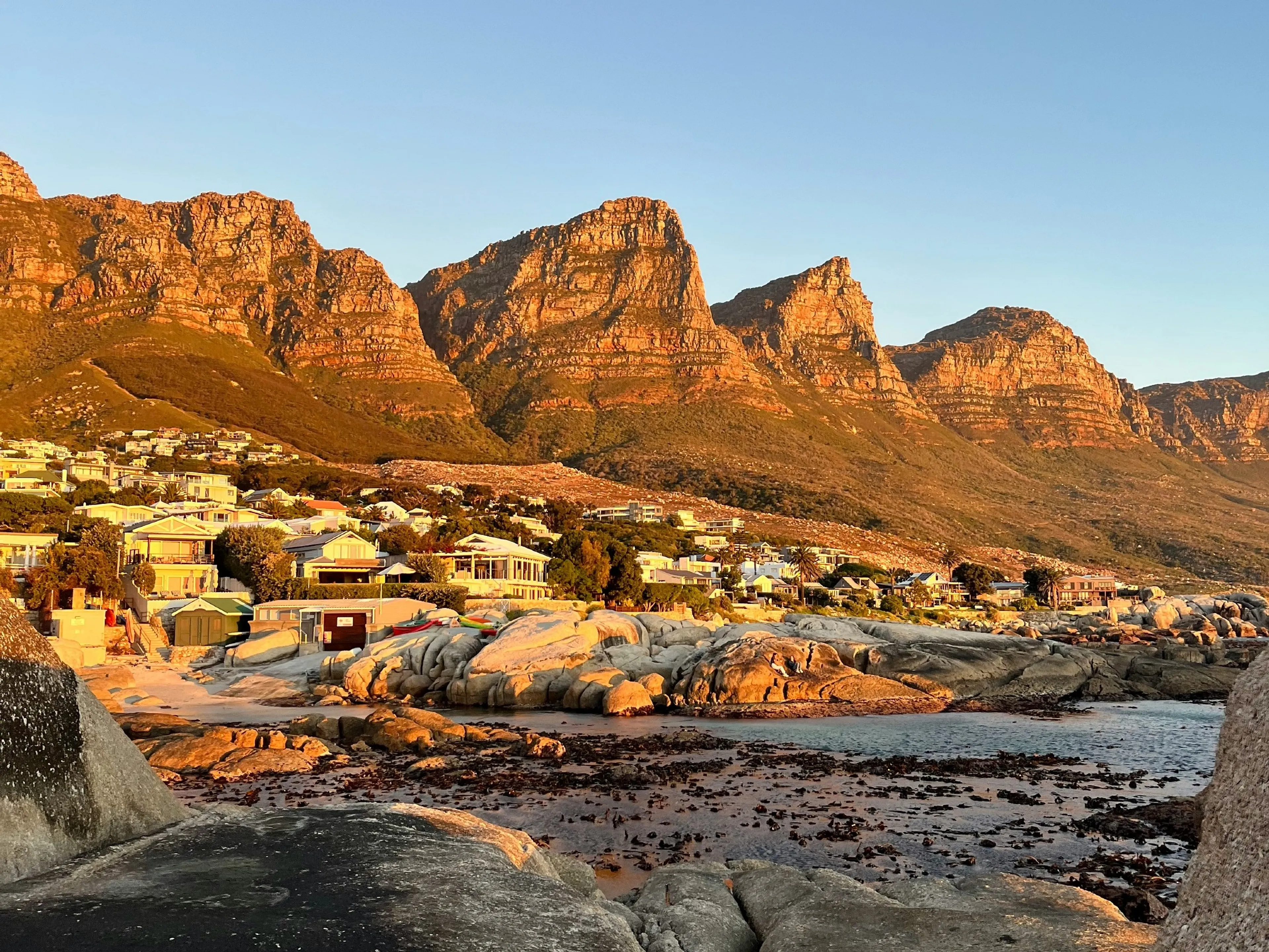 Golden light bathes the Twelve Apostles mountain range and the coastal houses of Cape Town.