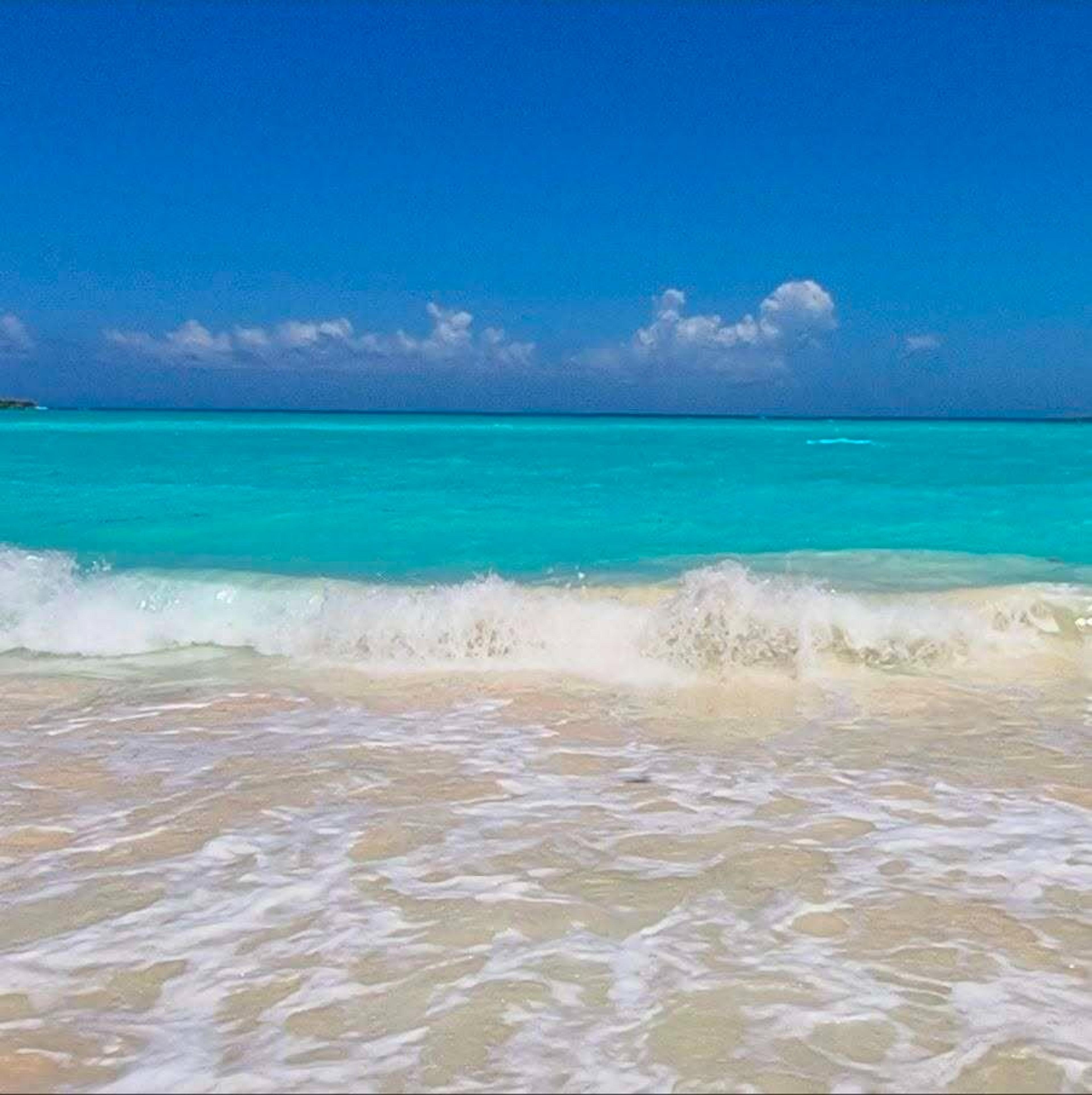 Crystal clear turquoise waves gently crash onto the sandy beach
