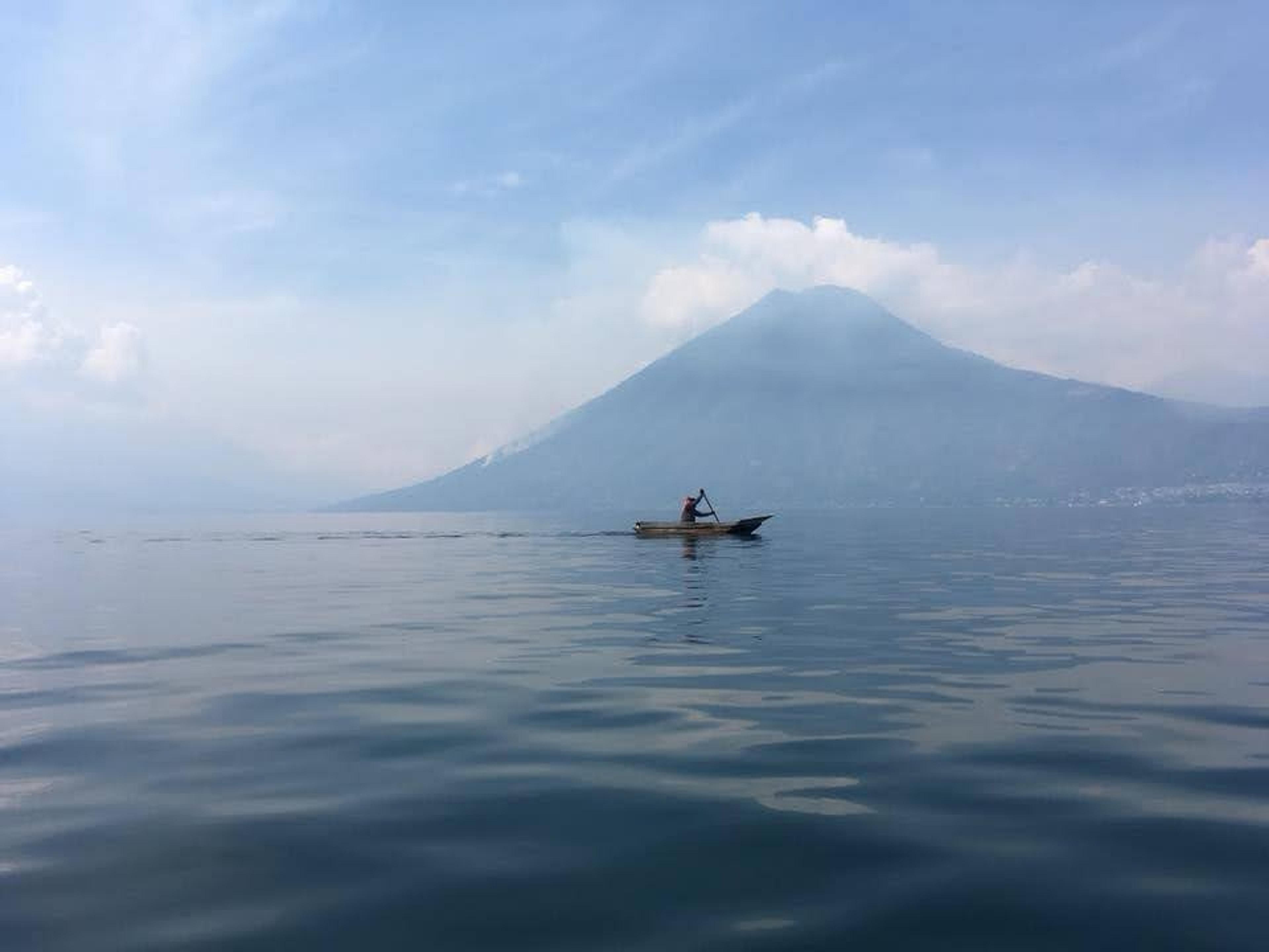 A lone boat navigates the tranquil waters of Lake Atitlán in Guatemala, with a majestic volcanic backdrop.