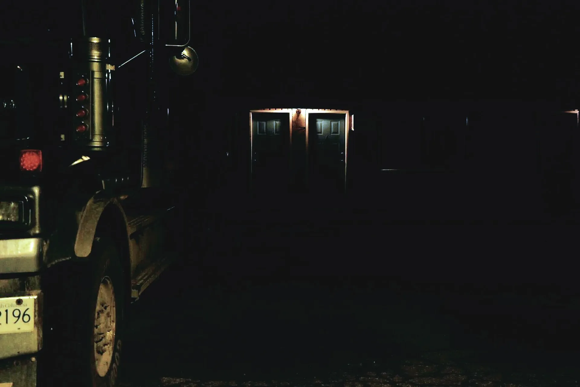 A motel door in the night illuminated by flickering light and a truck parked outside