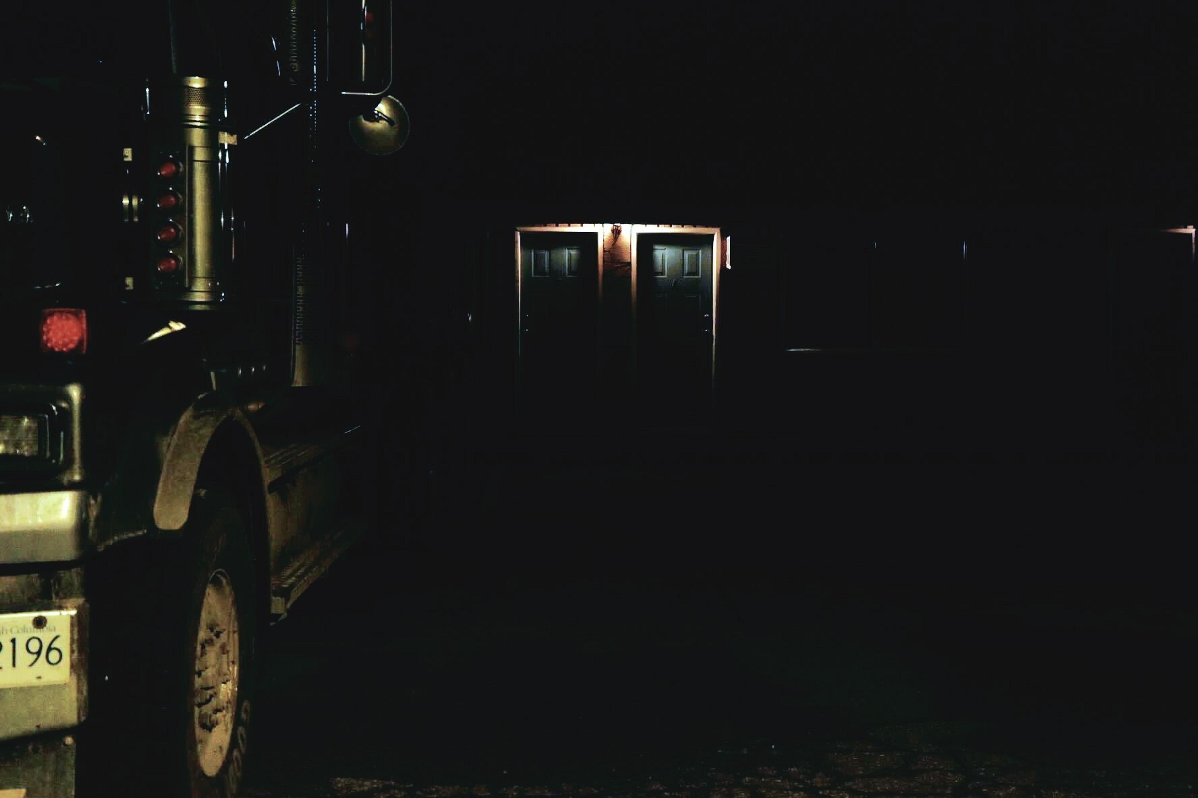 A motel door in the night illuminated by flickering light and a truck parked outside