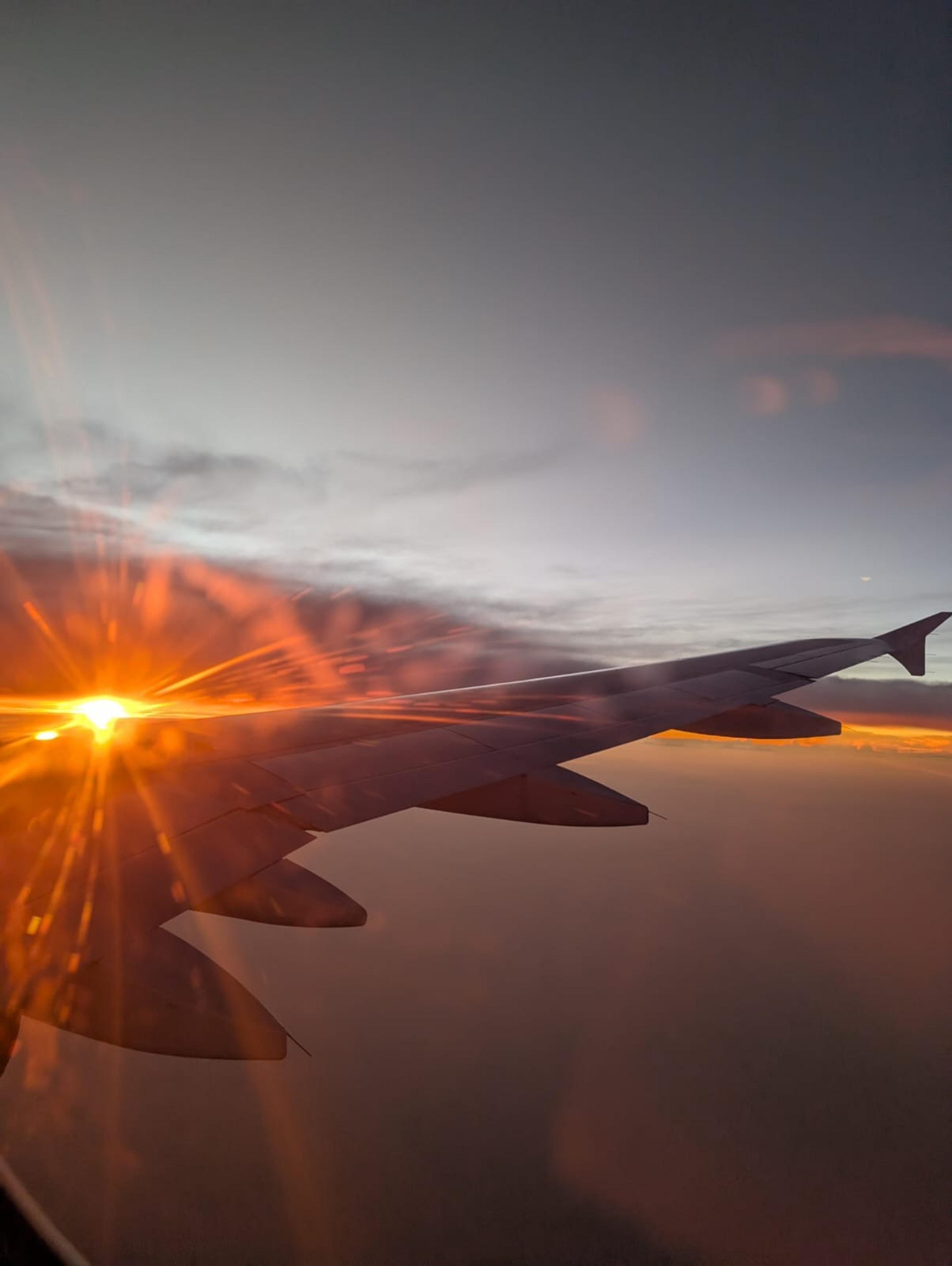 A vibrant sunset casts a warm glow over the wing of a Chine Eastern airplane, high above the clouds.