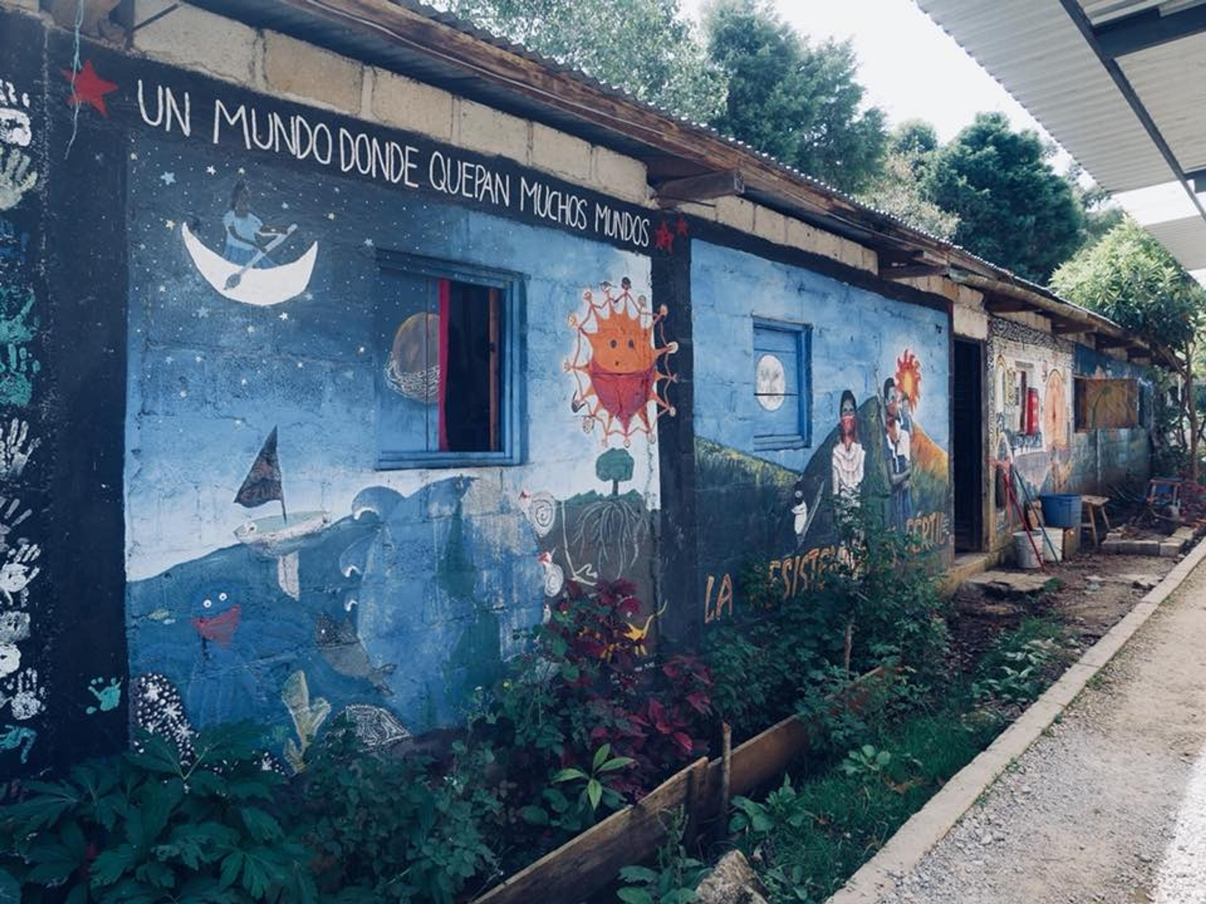 Bright and colorful murals adorn the walls of a rural building in Chiapas, Mexico, featuring themes of nature and community.