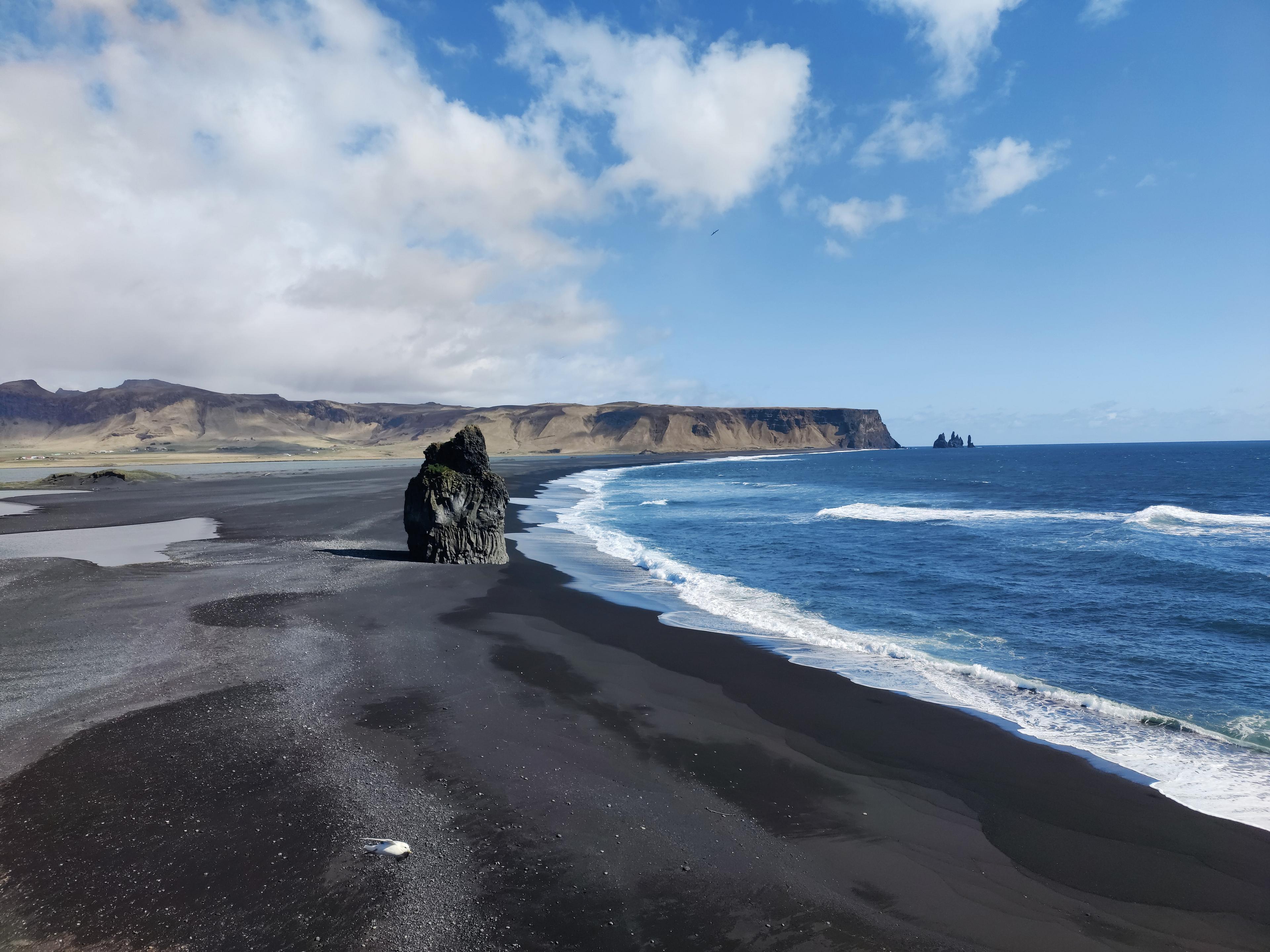 Reynisfjara, the iconic black sand beach in Iceland, features dramatic basalt sea stacks framed by azure waters and rugged cliffs. 