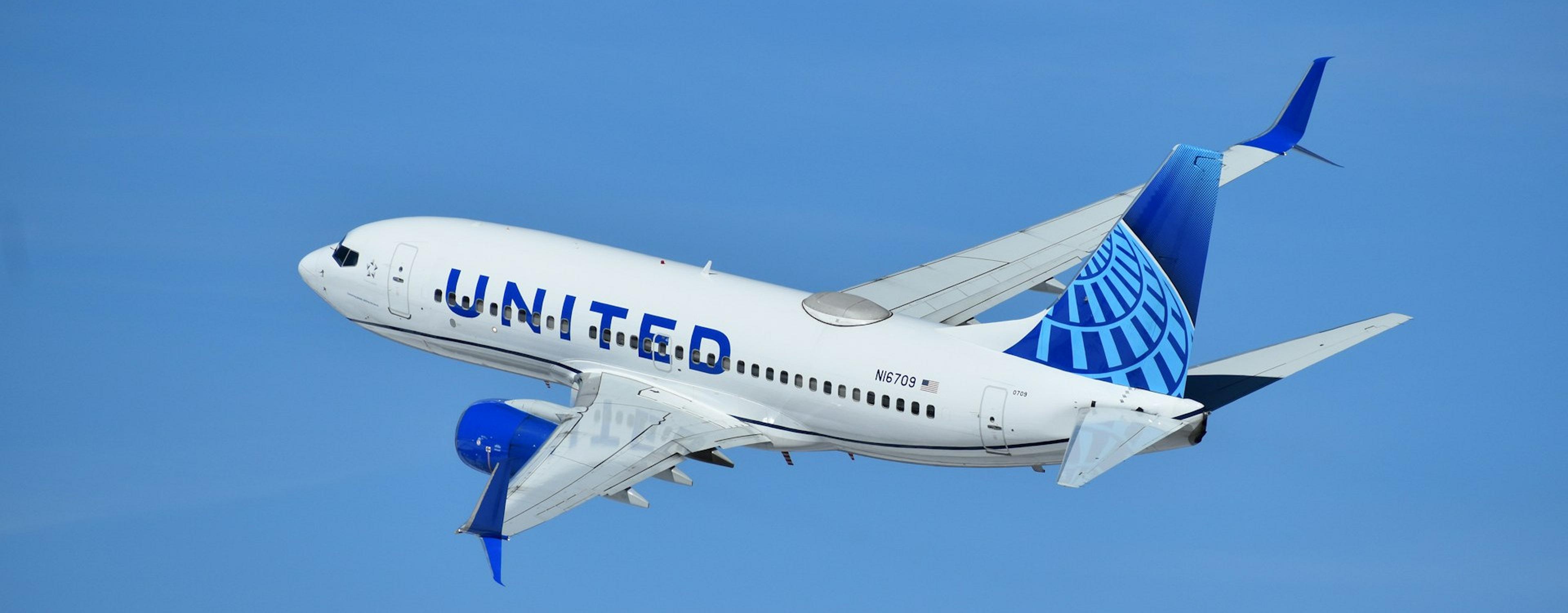 A United Airlines plane ascends against a bright blue sky, likely during takeoff or landing at a major airport.