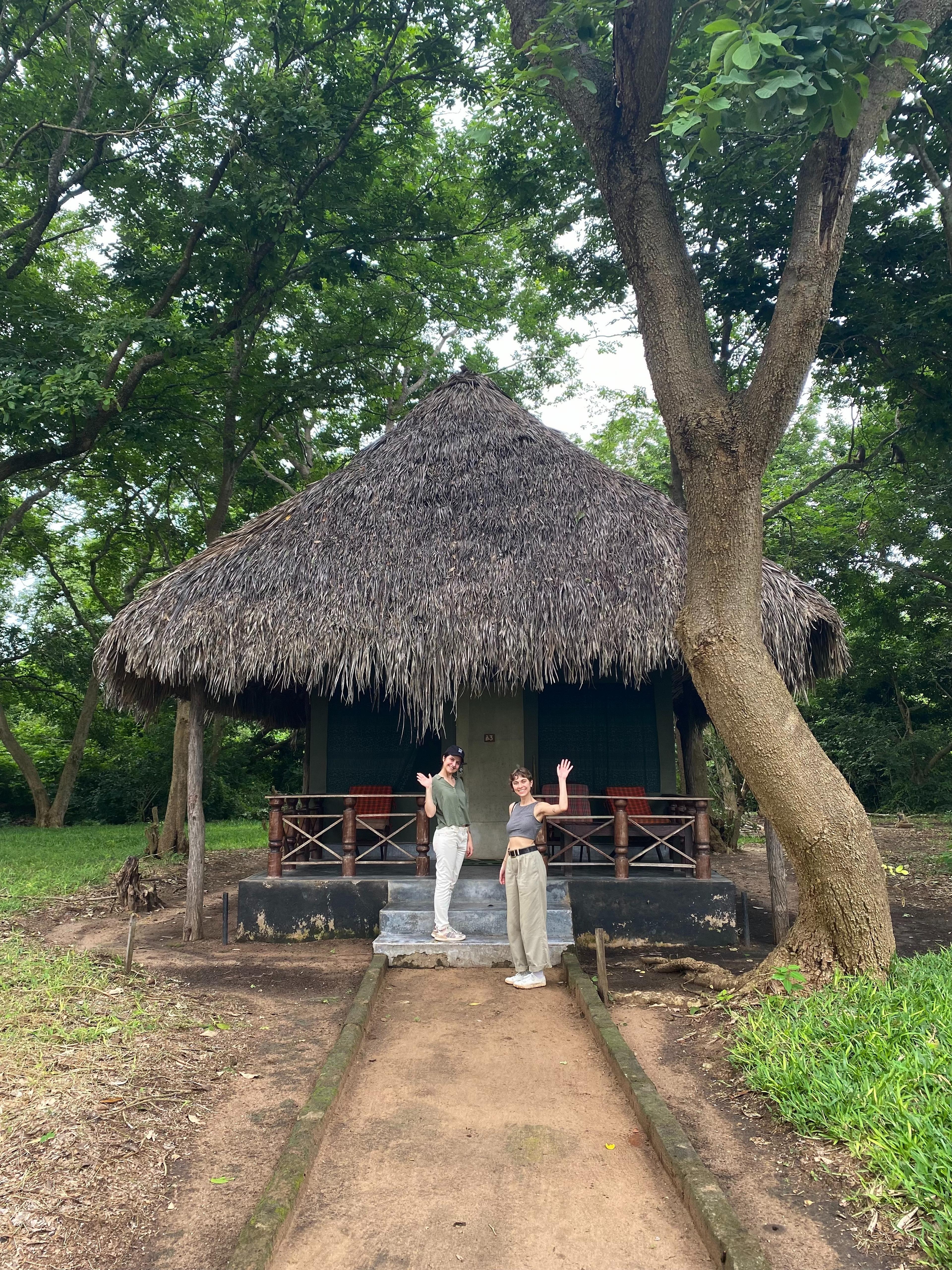 Fran and Andreia waving outside a hut