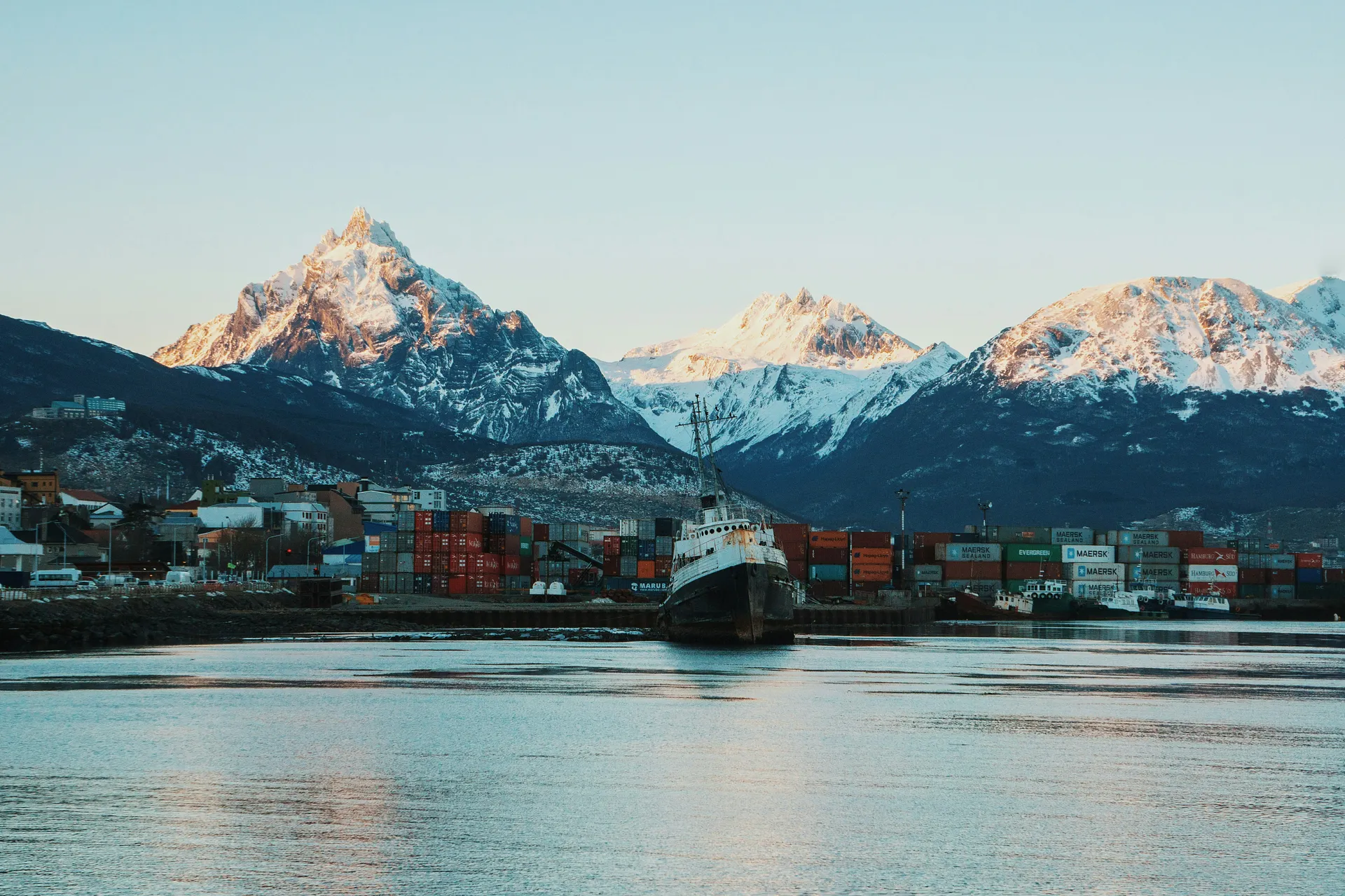 A harbor with stacked shipping containers and a ship set against the backdrop of snow-capped mountains in Ushuaia, Argentina.
