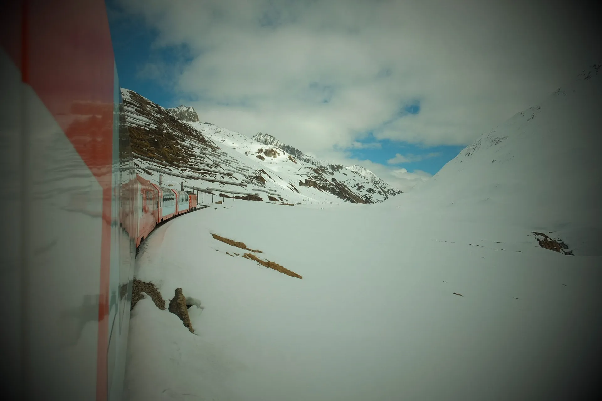 A train curves through the snowy landscape of the Swiss Alps near the Bernina Pass.