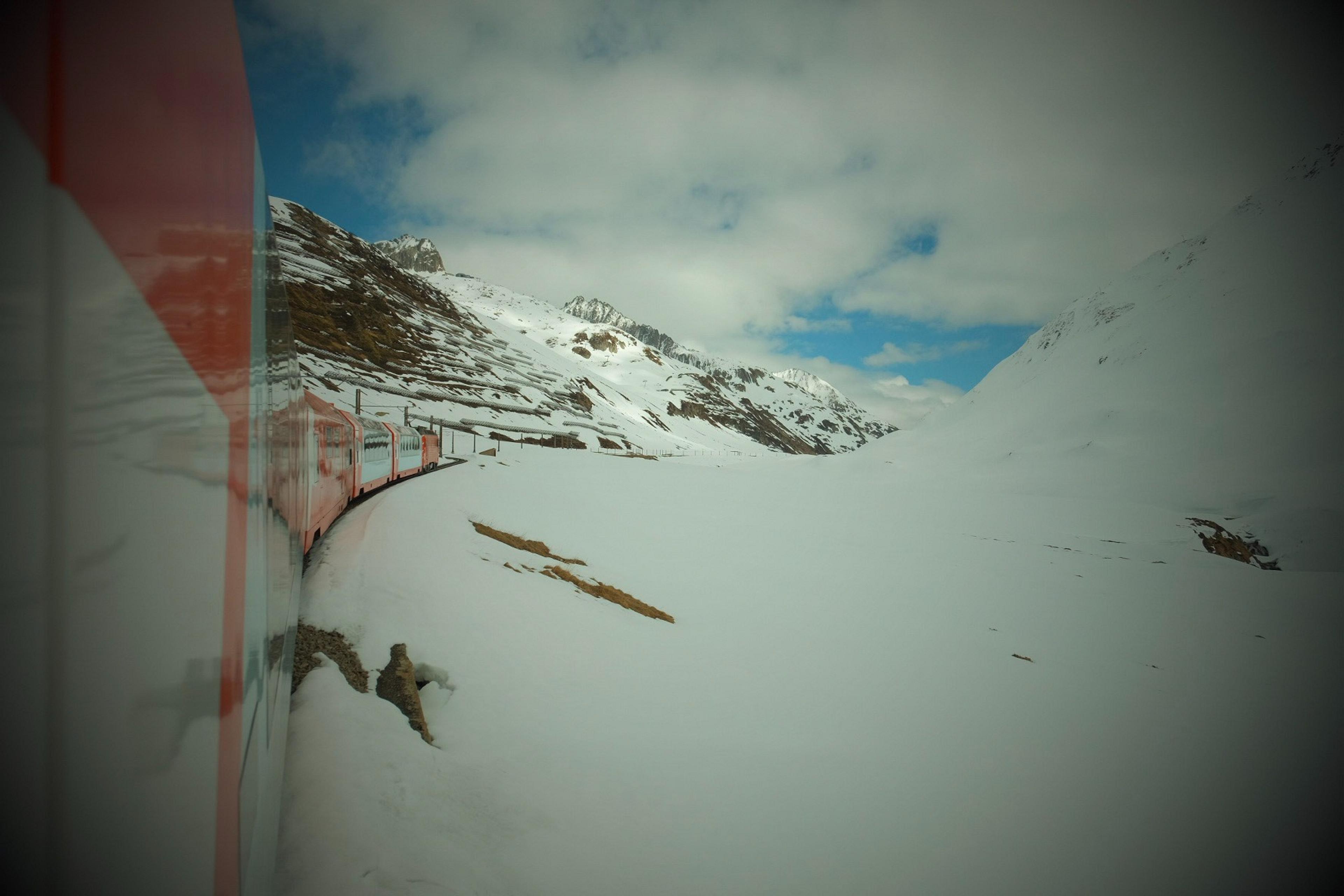 A train curves through the snowy landscape of the Swiss Alps near the Bernina Pass.