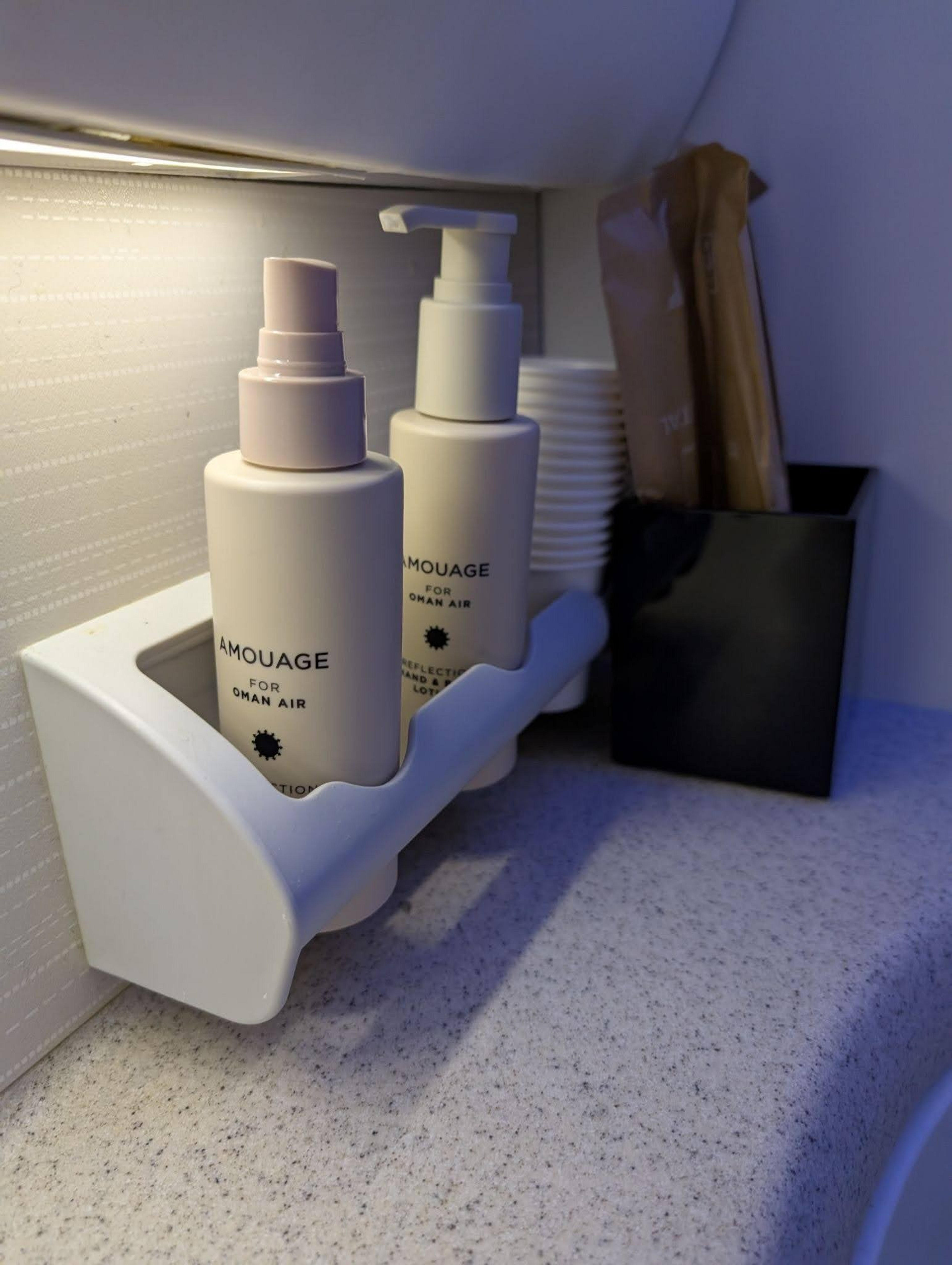 A compact shelf in an Oman Air airplane restroom contains Amouage products.